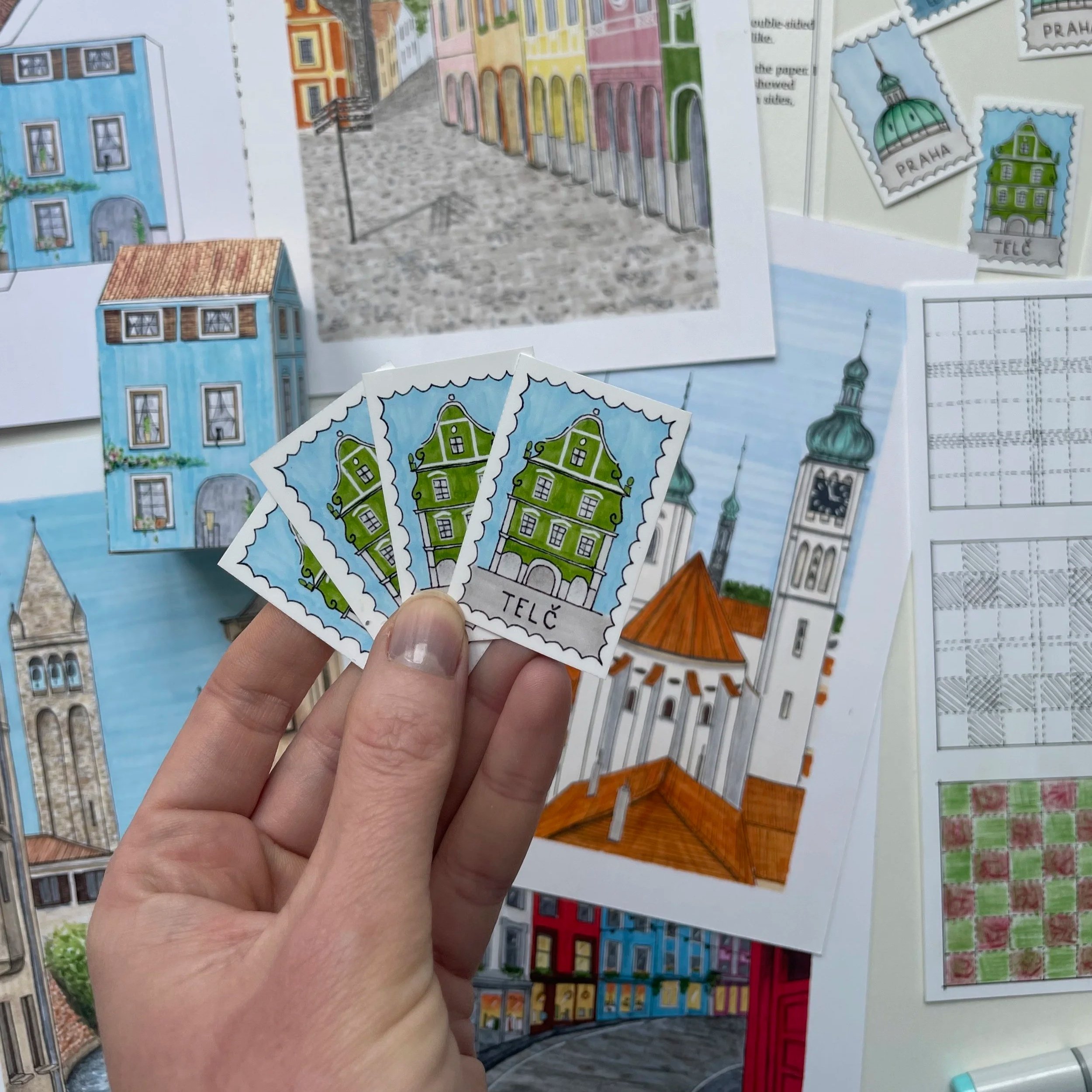 Close-up of a hand holding a sheet of colorful stickers depicting buildings with different architectural styles and colors, on a background of similar stickers arranged on a surface.
