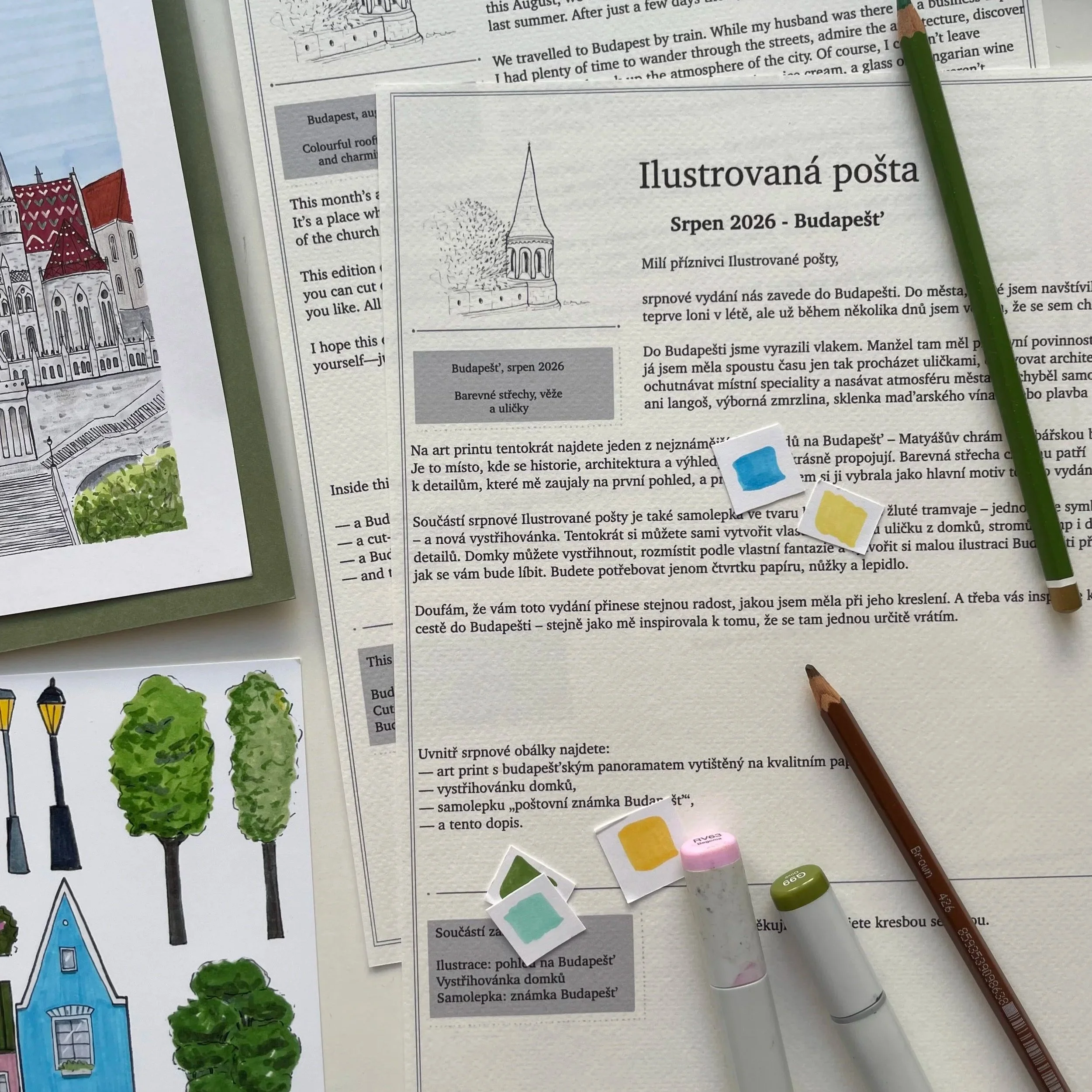 Several illustrated pages of a publication about Budapest, with drawings of buildings and trees, green markers, and colored paper swatches on a table.