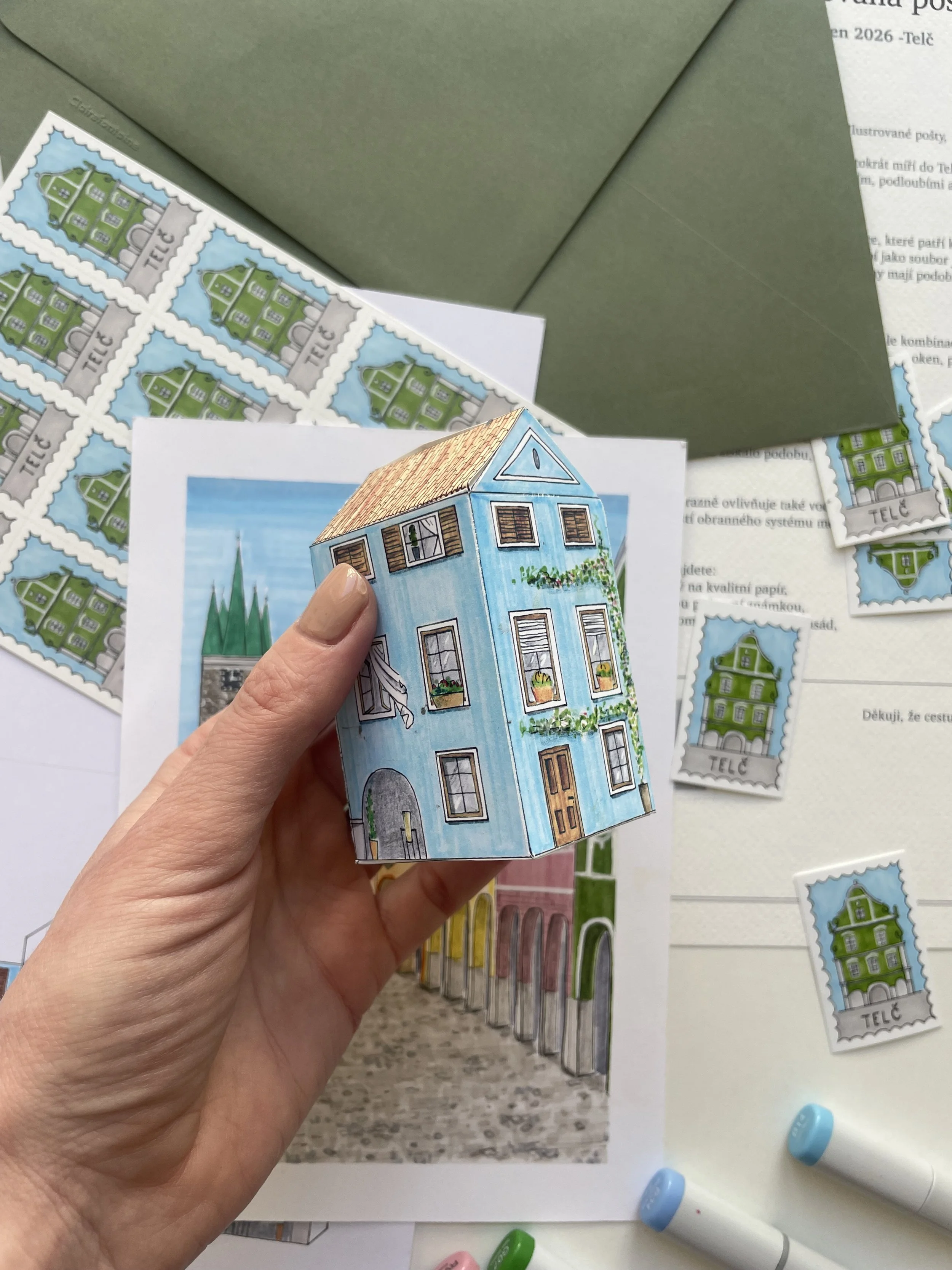 A hand holding a paper cutout of a blue house with windows and a door, in front of a desk with various colored stamps and papers.