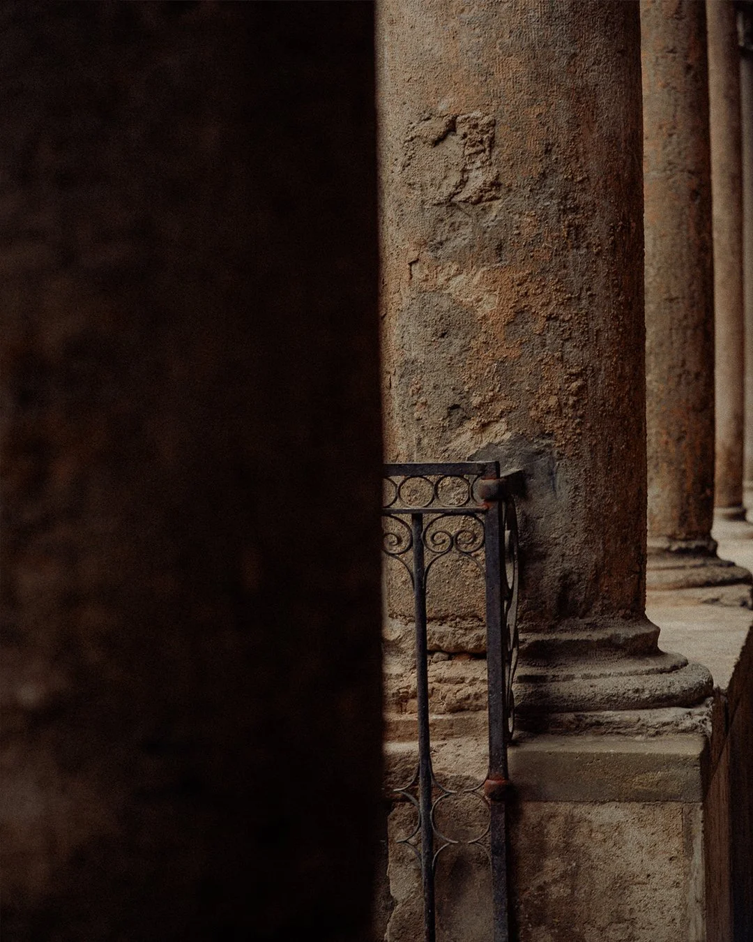Close-up of ancient stone columns and a decorative metal railing, with shadows and textured surfaces.