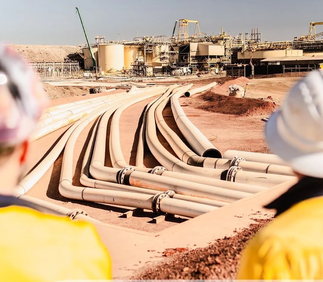 View of pipelines and construction workers on an oil or gas drilling site.