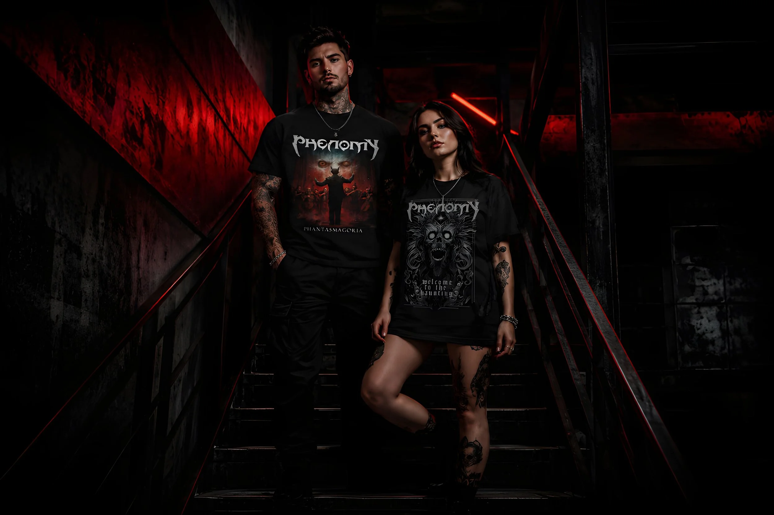 A young man and woman standing on a dark staircase with red and black lighting, wearing black graphic T-shirts and tattoos visible.