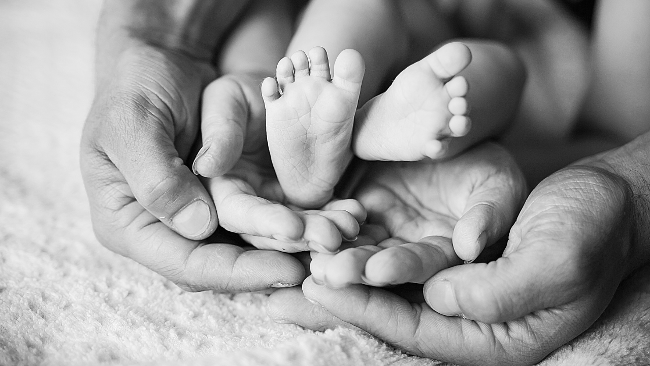 Nahaufnahme von Händen, die eine kleine babyartige Figur halten, im schwarzen und weißen Filter.
