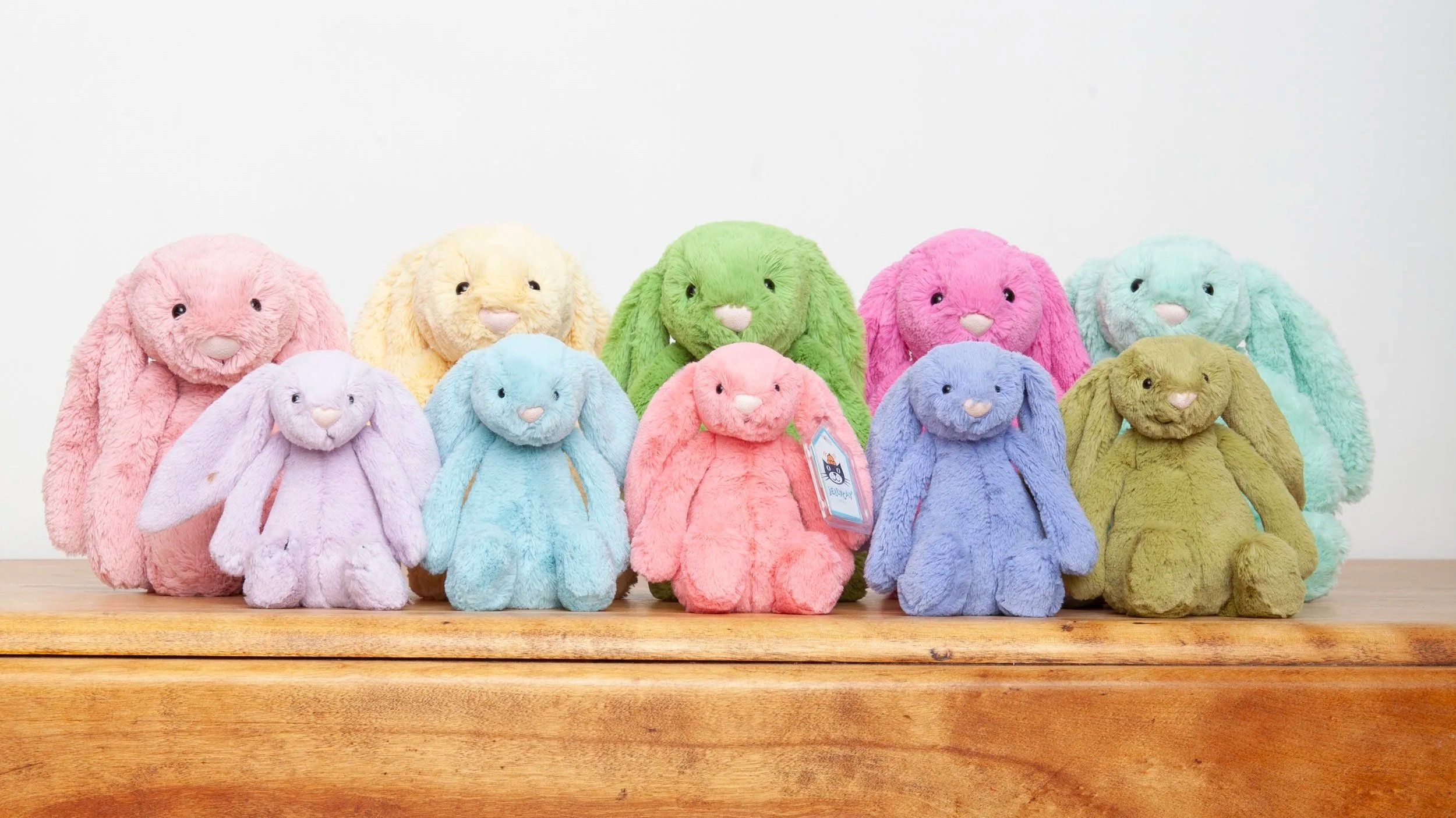 A collection of colorful plush bunny stuffed animals arranged on a wooden surface against a plain white background.