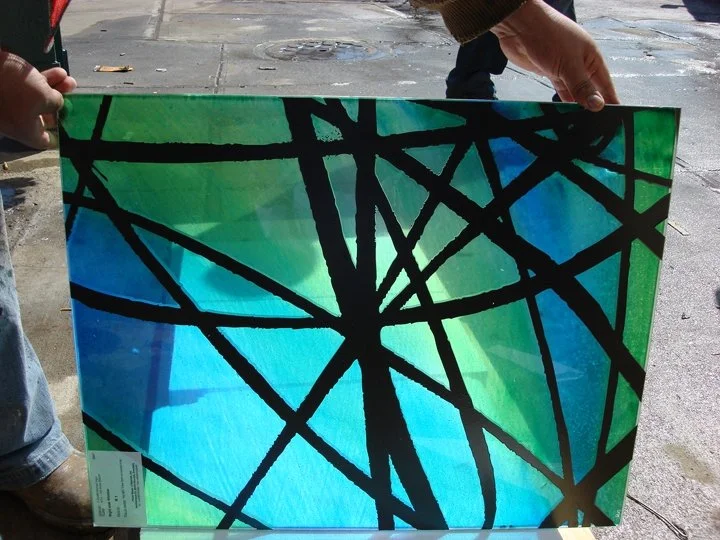 Person holding a colorful, abstract art piece with black intersecting lines on a green, blue, and teal background.
