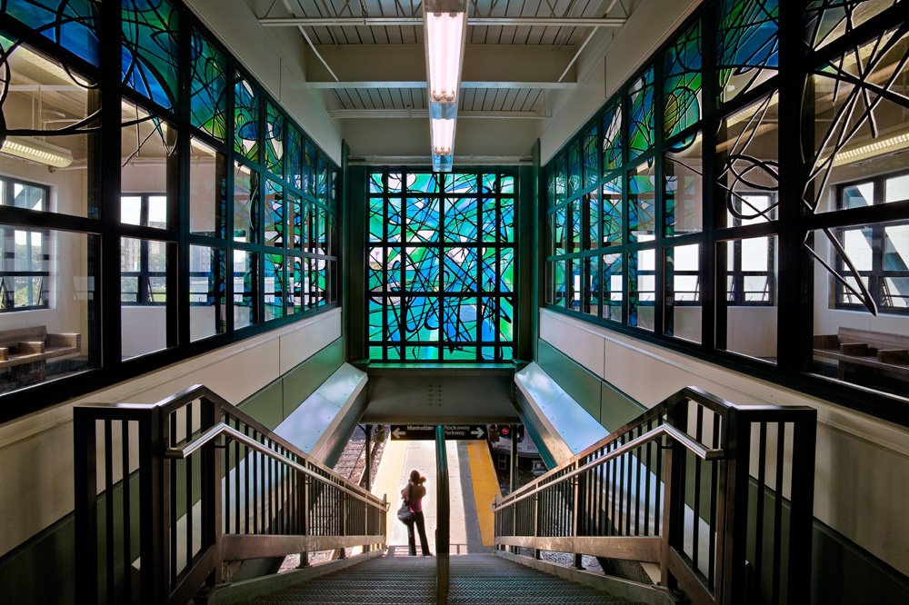 Interior view of a subway station stairway with stained glass windows and a woman standing at the base.