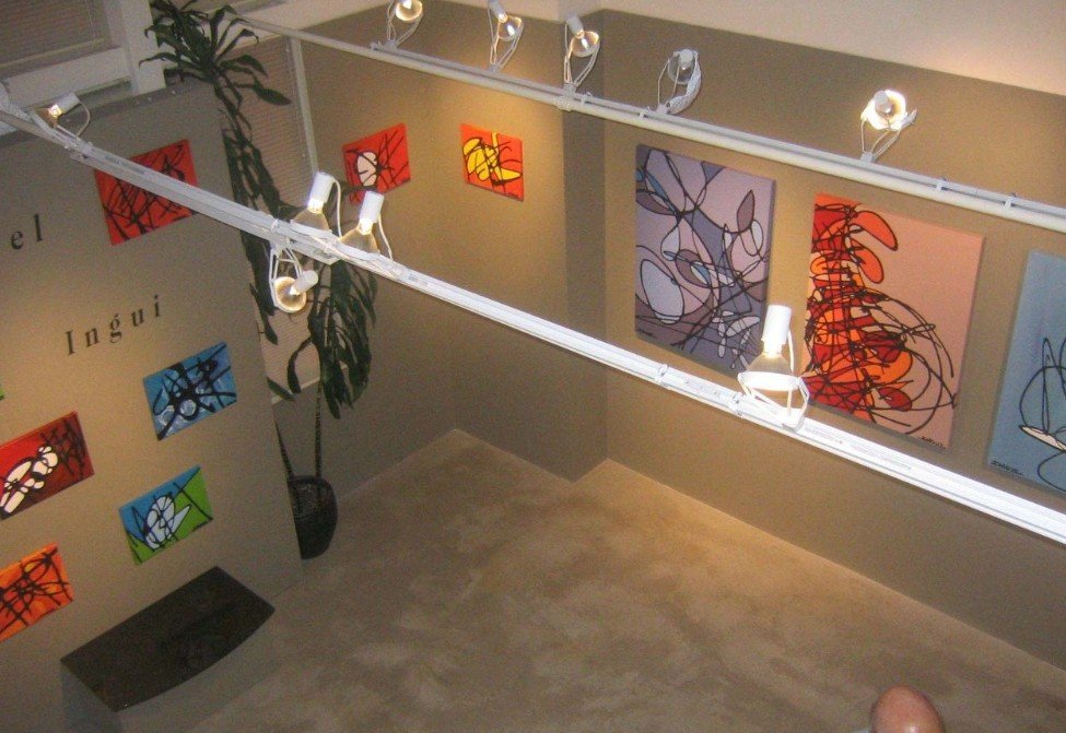 View of an art gallery with abstract paintings on the walls, track lighting, and a potted plant in the corner.
