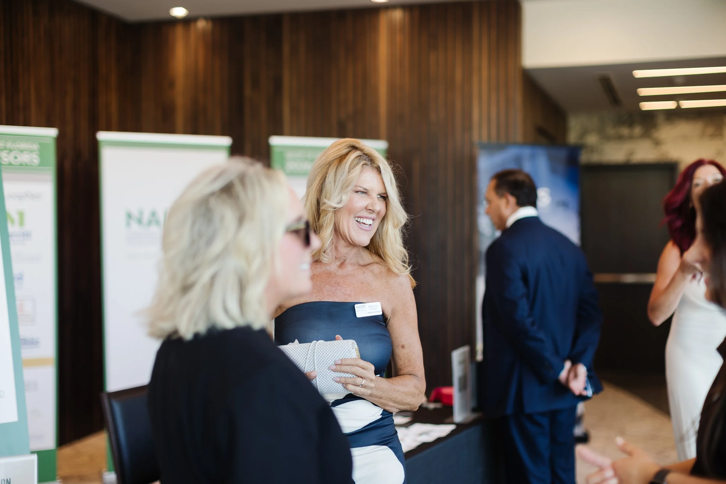 Women engaging in conversation at a professional event, with information posters in the background.