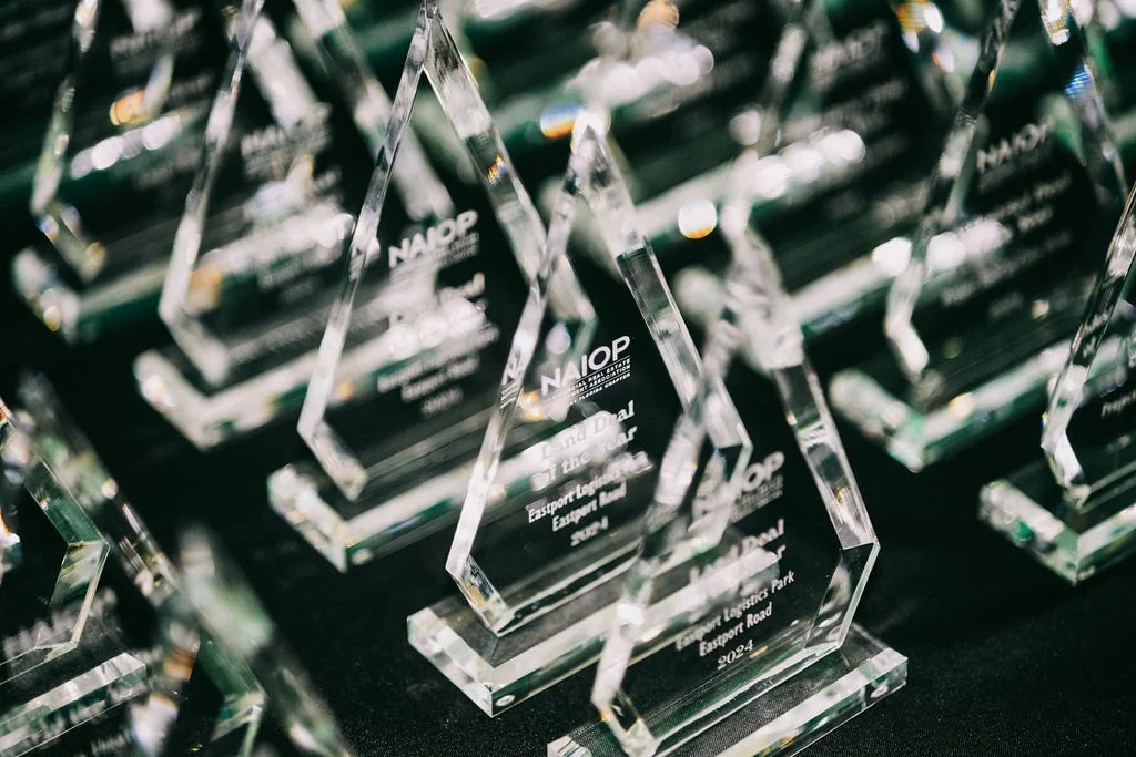 Multiple glass awards arranged on a black surface, engraved with 'NAIOP' and other text