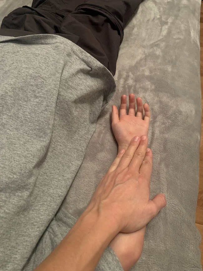 Un bébé allongé sur le ventre, recevant un massage ou une thérapie par une personne adulte, probablement un thérapeute, dans une pièce intérieure.