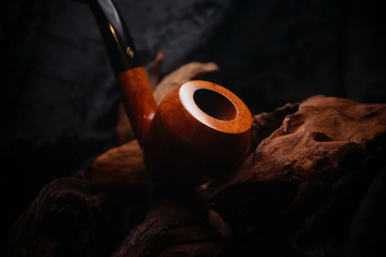 A wooden smoking pipe resting on a rough, textured piece of wood, shown in a low light setting.