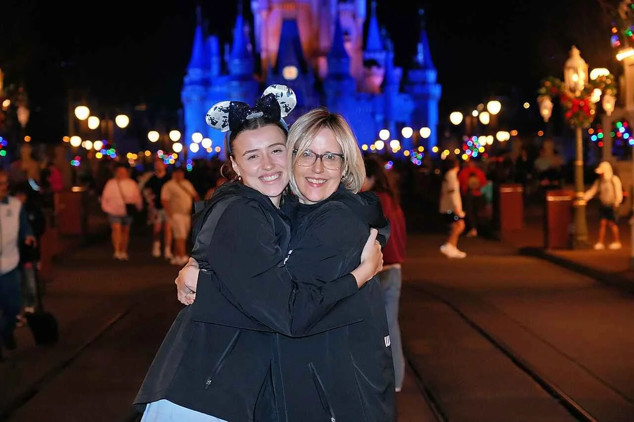 Young woman and mid-aged woman hugging on main street in front of the castle at night