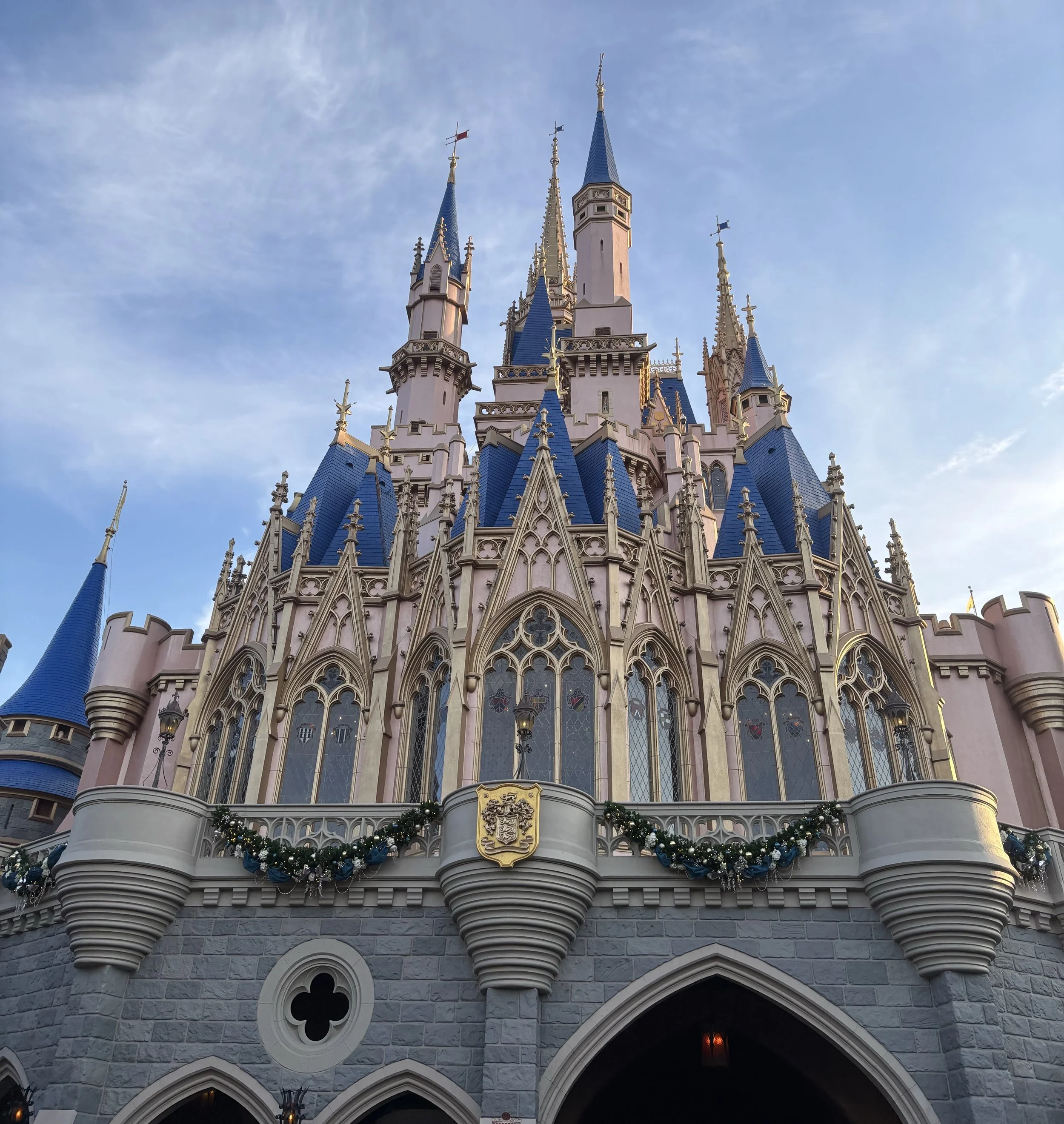 The backside of Cinderella's castle taken from the ground. The stain glass windows of the restaurant and gold and blue turrets on the blue sky.
