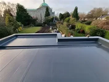 View of a flat rooftop with a ledge overlooking a lush garden and a church with a green dome in the background.