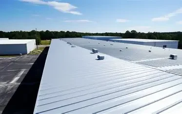 View of a large white metal rooftop with vents, under a partly cloudy sky.