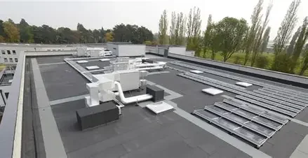 Rooftop with HVAC systems, vents, and solar panels under a cloudy sky, with trees in the background.