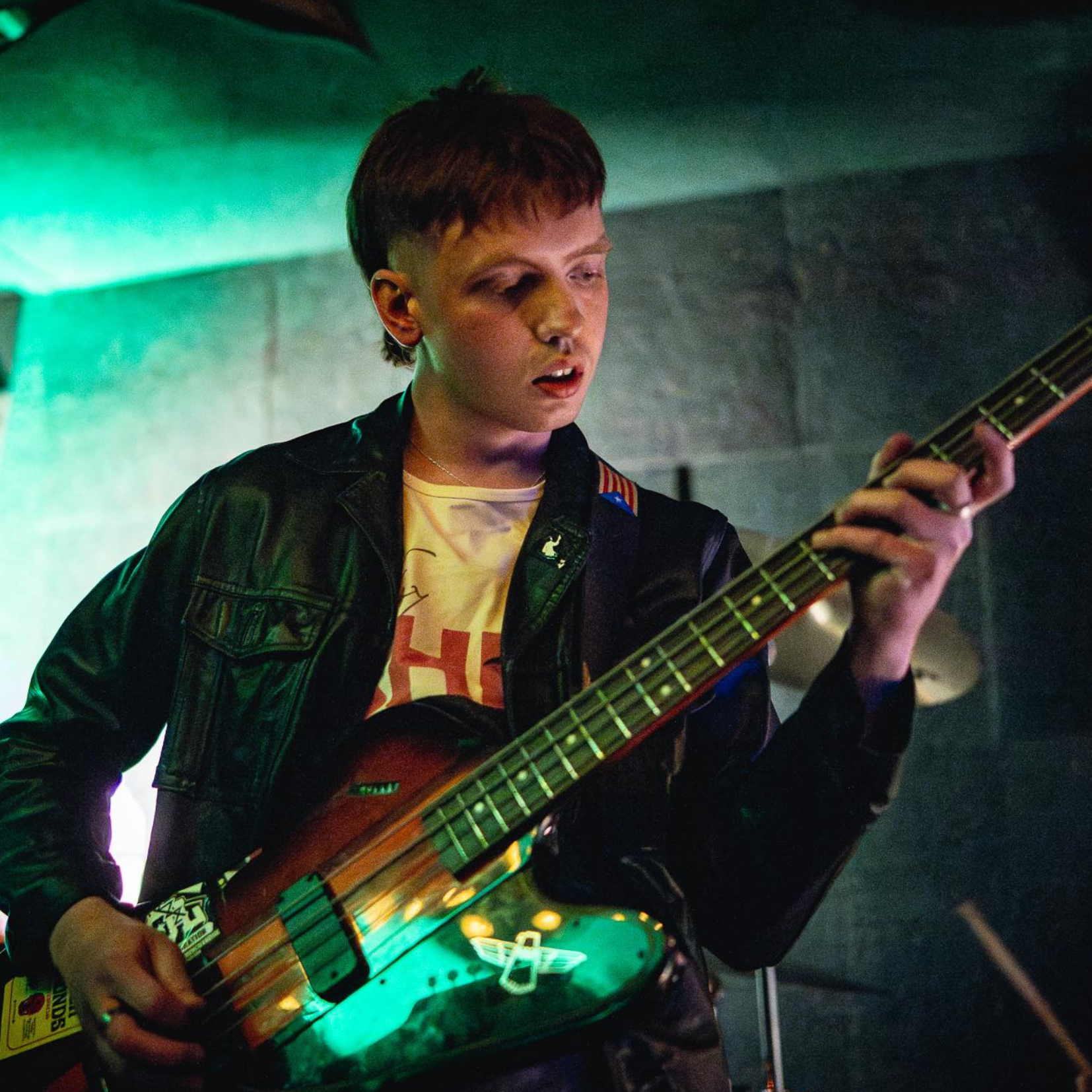 A young person playing an electric guitar with glowing lights underneath it, standing in a dimly lit room.