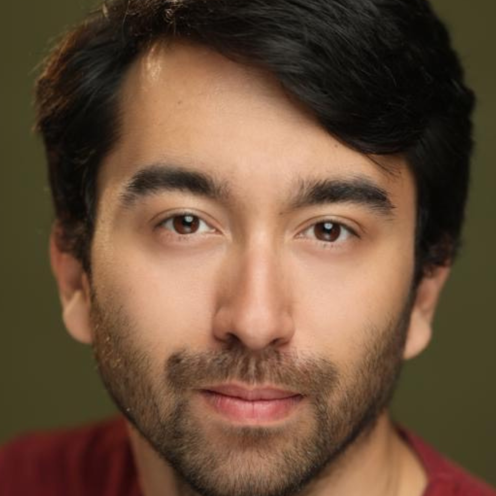 Close-up of a man's face showing brown eyes, dark hair, and slight beard, with a neutral expression.