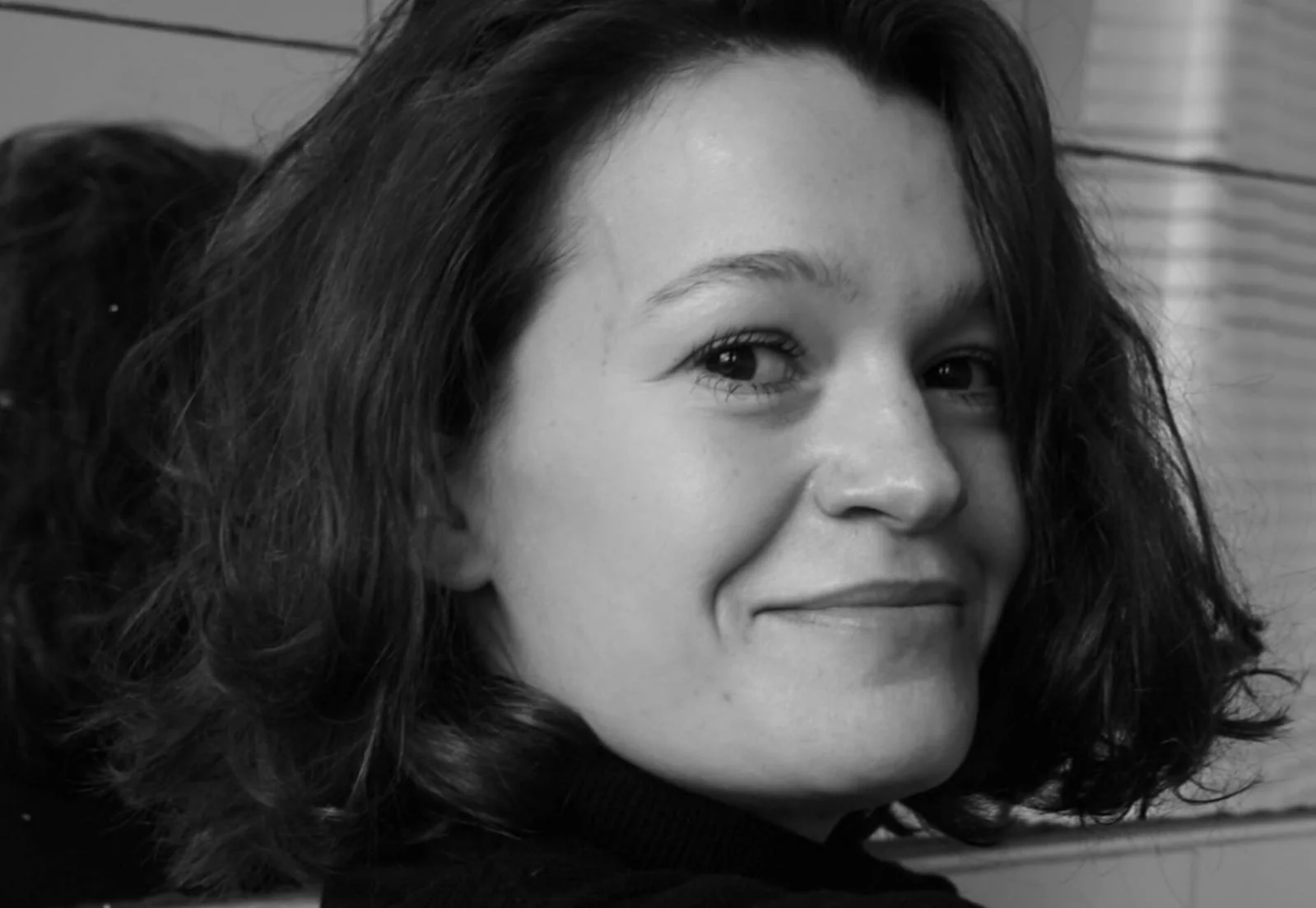 A young woman with dark, wavy hair smiling at the camera in black and white.