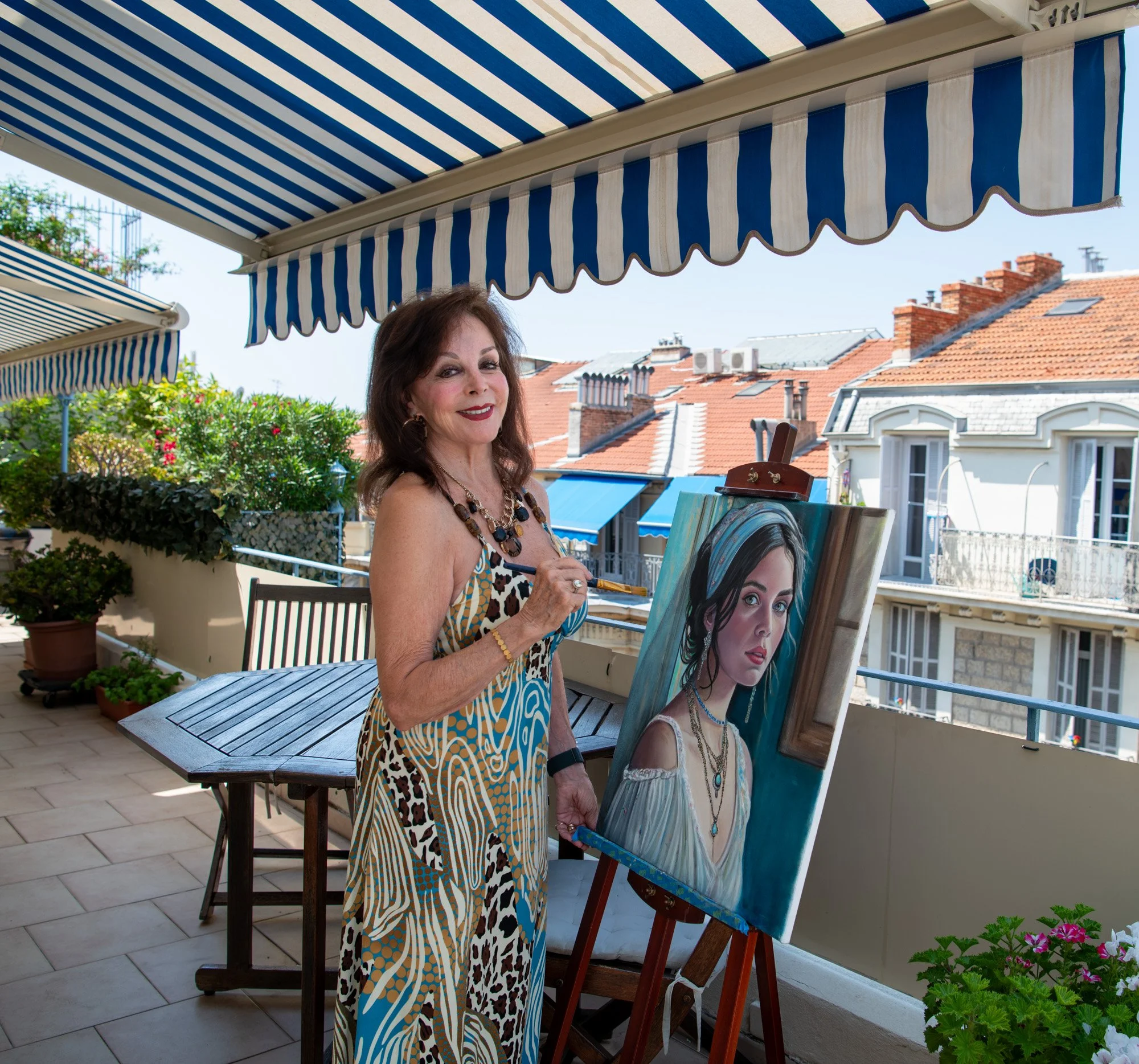 Fay Stassis Vernon today, on her balcony in Nice, France, beside one of her oil portraits