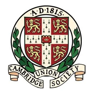 The shield of the Cambridge Union Society featuring a red and white crest with a crown, four lions, and a central cross, surrounded by green laurel branches, with the inscription 'A.D. 1815' and a banner reading 'Cambridge Union Society'.