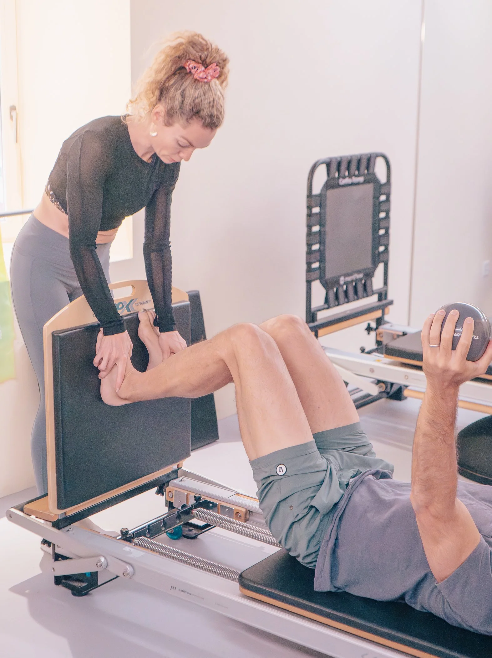 Physical therapist assisting an elderly person with a leg exercise on a specialized treatment table, with exercise equipment nearby.
