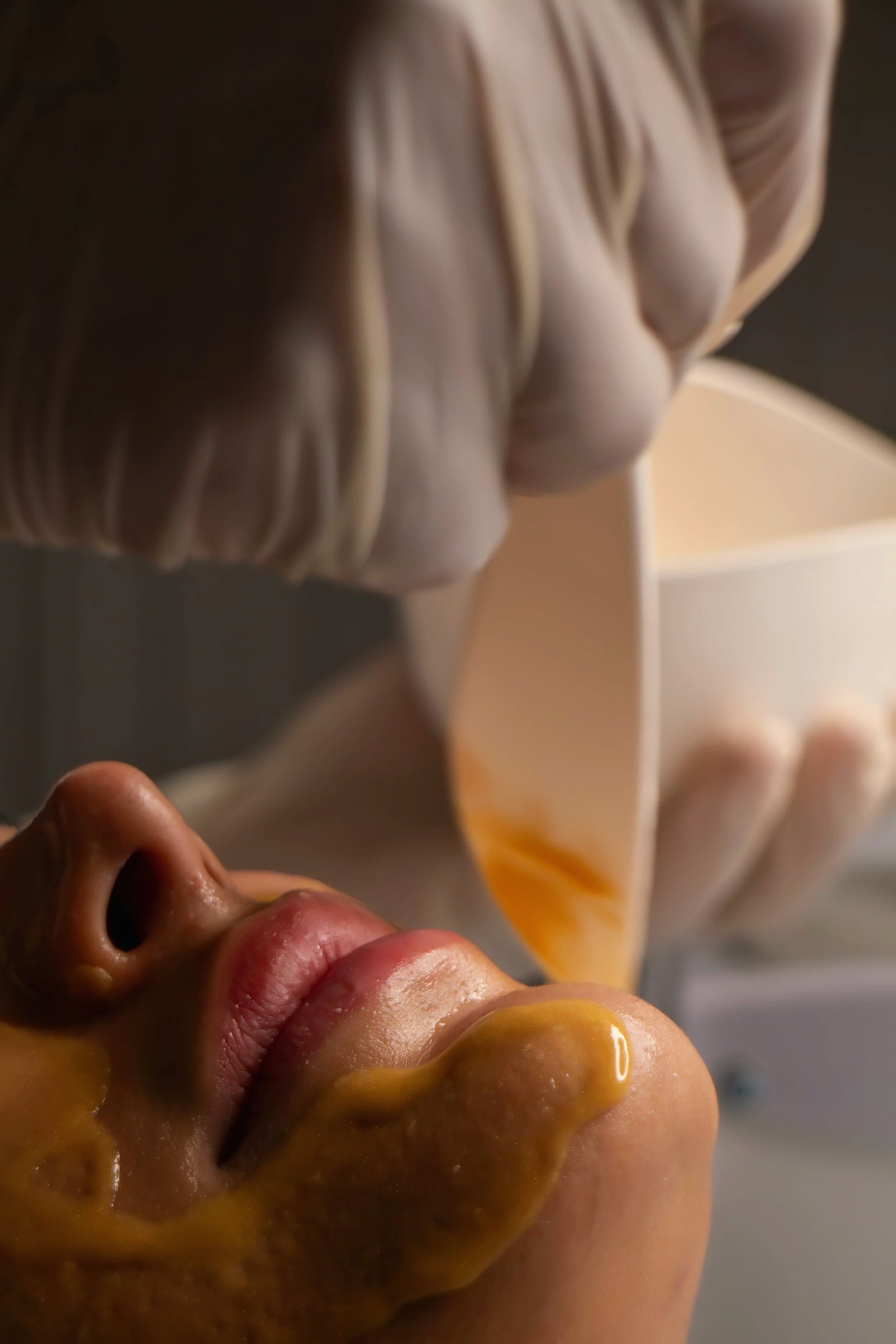 A clinician applying an amber-toned chemical skin peel treatment to a client's face with a brush