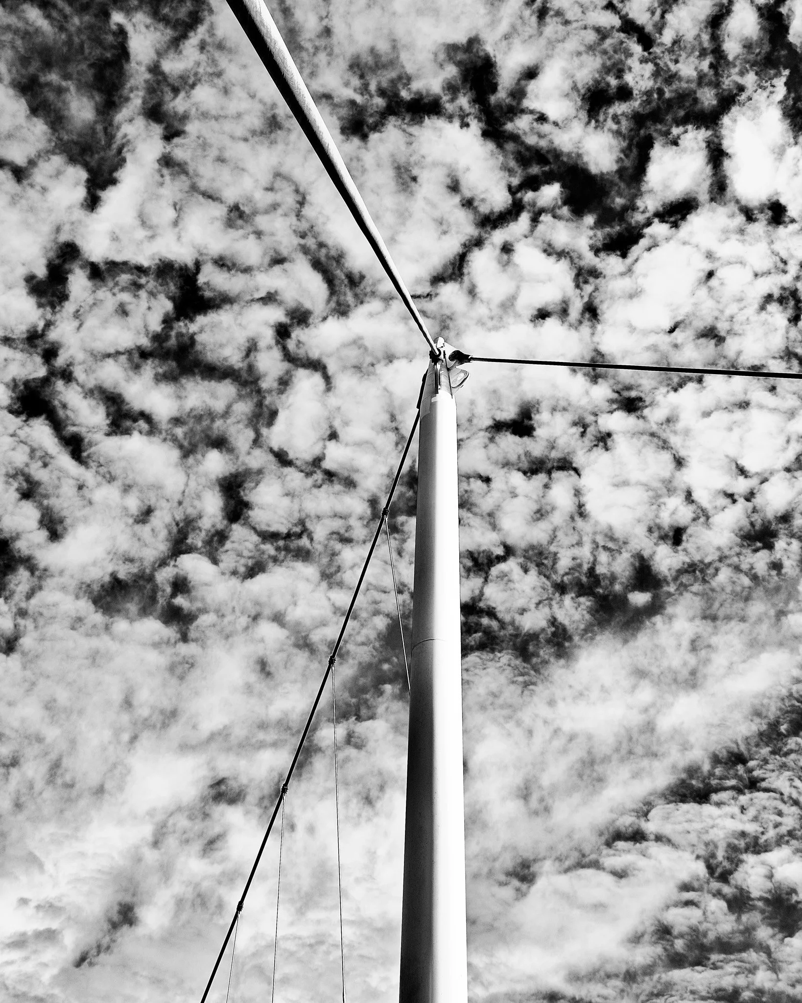 Black-and-white upward view of a wind turbine against a cloudy sky