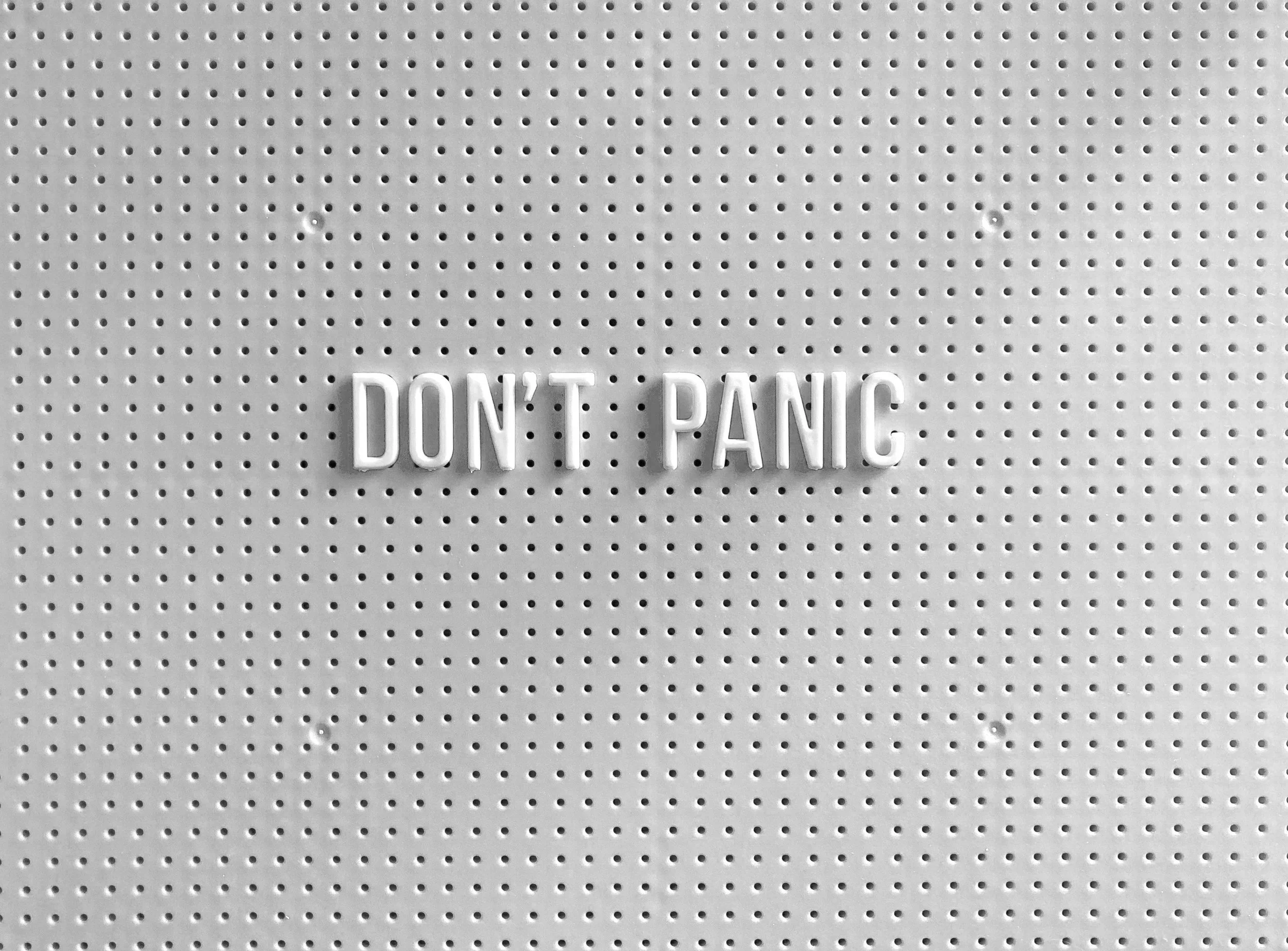 White plastic sign with the words "DON'T PANIC" in raised letters