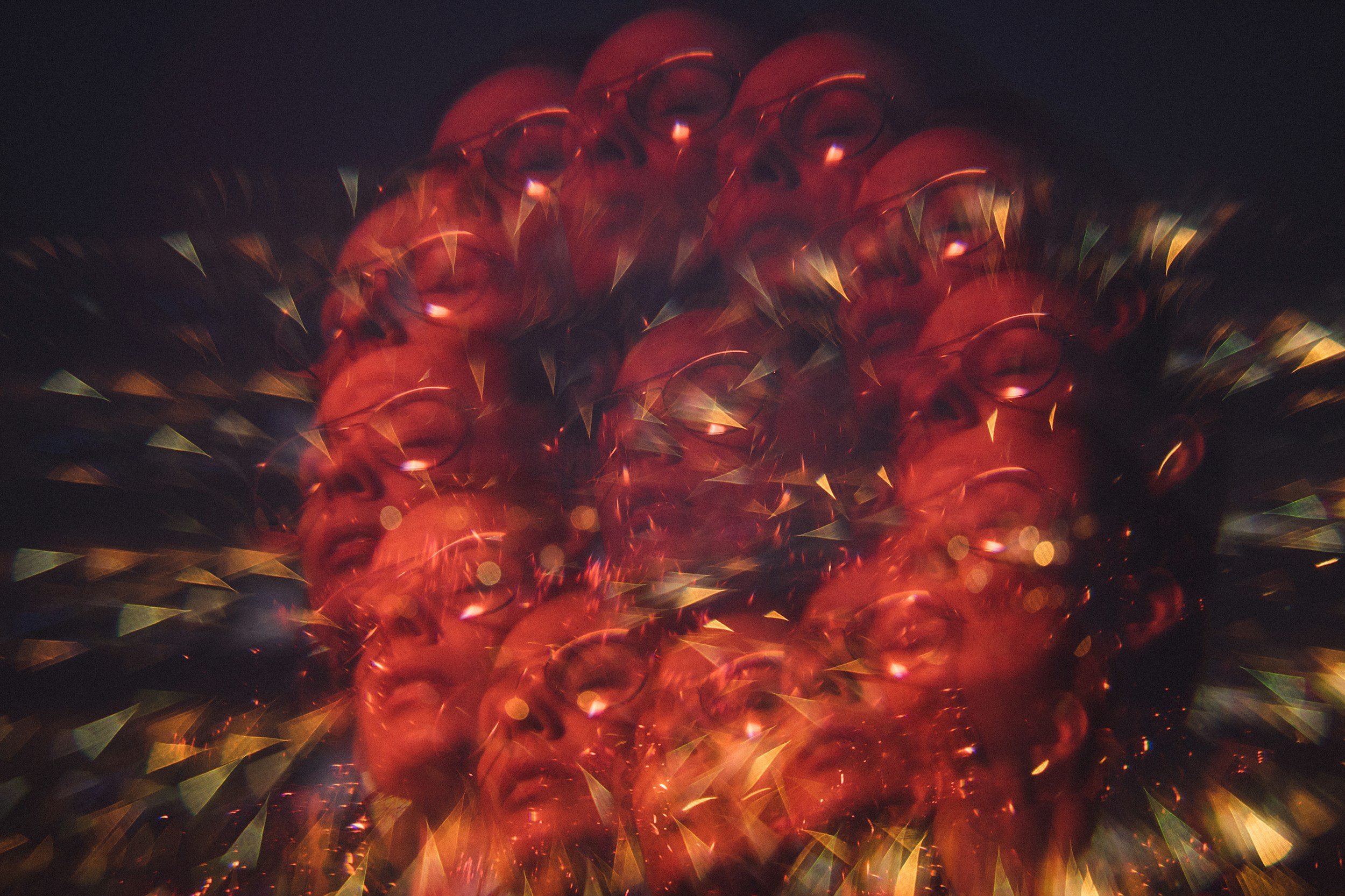 A display of red Christmas ornaments with a gold and green reflective finish, illuminated by string lights that create a warm glow and spark-like reflections.