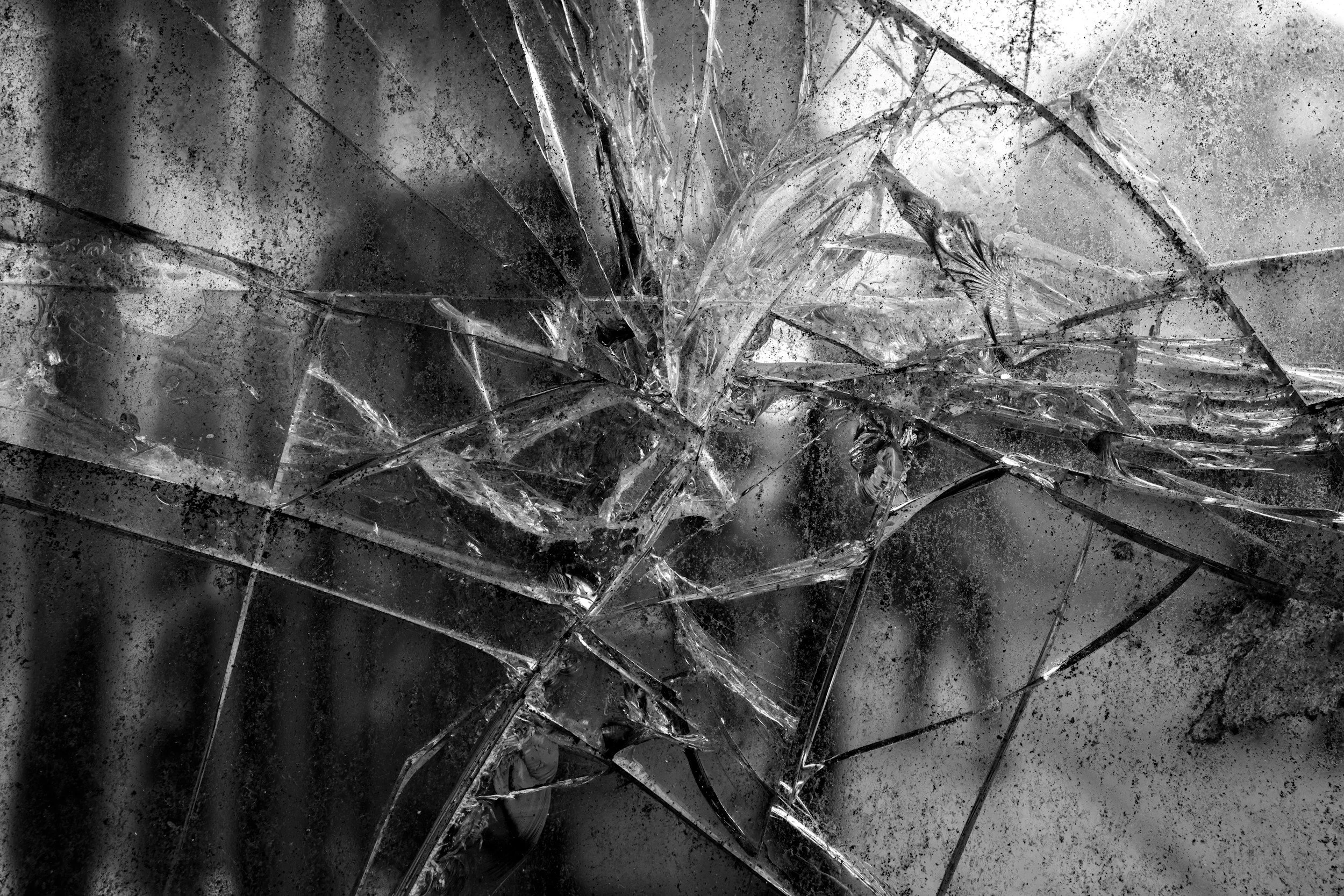 Shattered glass pieces with jagged edges and cracks on a dark surface.