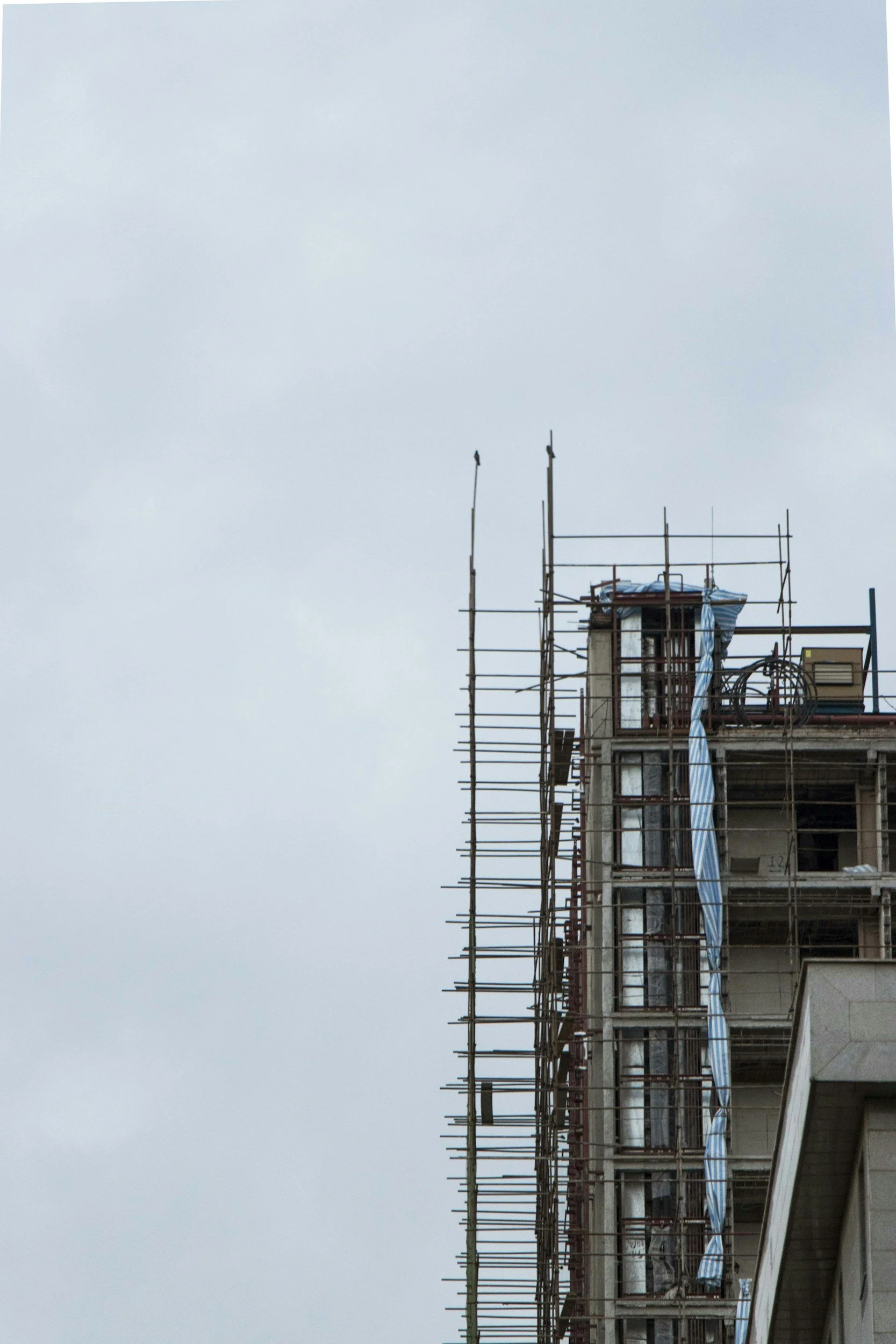 Part of a building under construction with scaffolding on a cloudy sky.