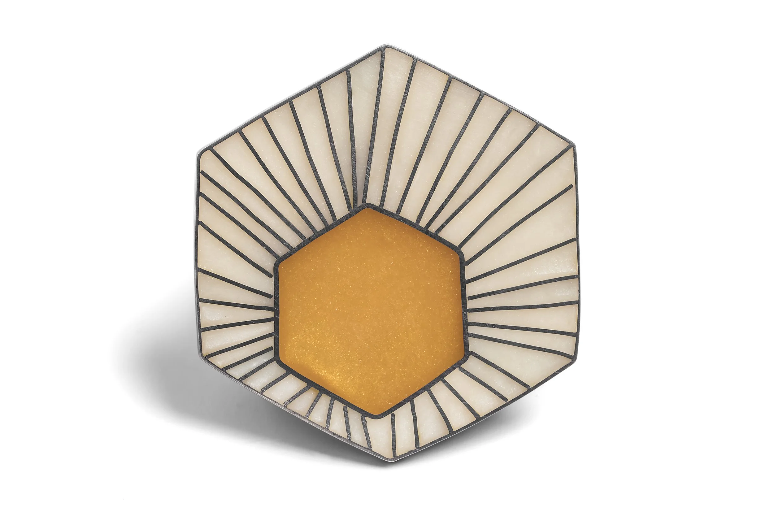 Close-up of a decoratively designed, hexagon-shaped candle with a black metal frame and cream-colored panels, featuring an orange-colored wax core.