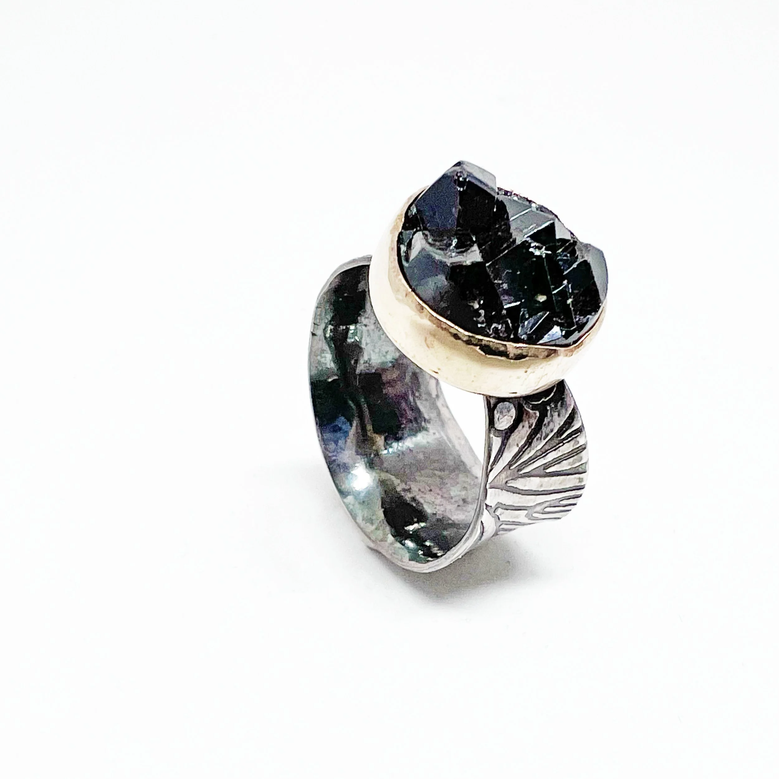 A black gemstone held between two fingers with a silver ring on the finger, against a white background.
