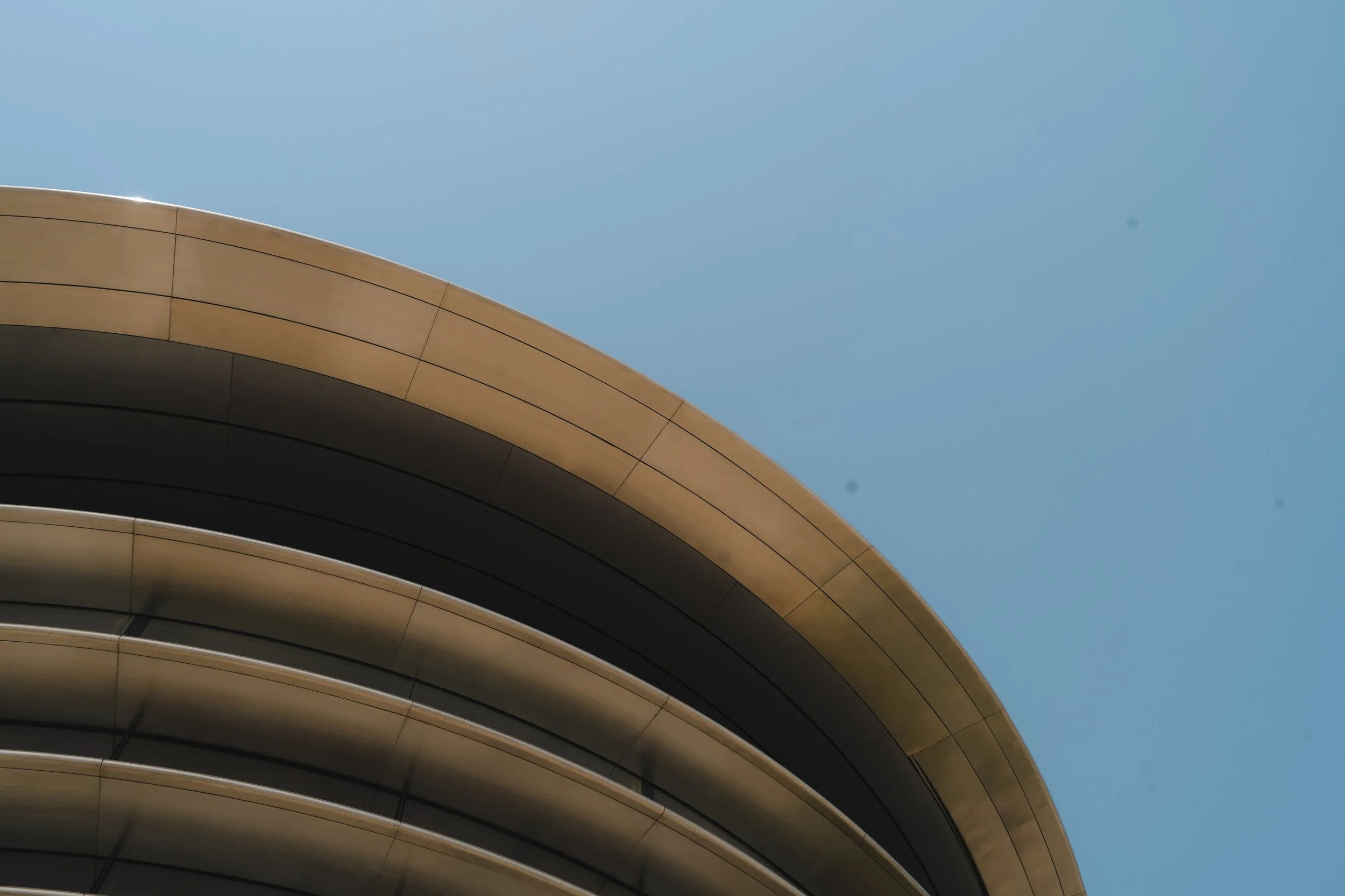 Vue partielle d'un bâtiment moderne avec une architecture fluide en forme de courbe, en dessous d'un ciel clair.
