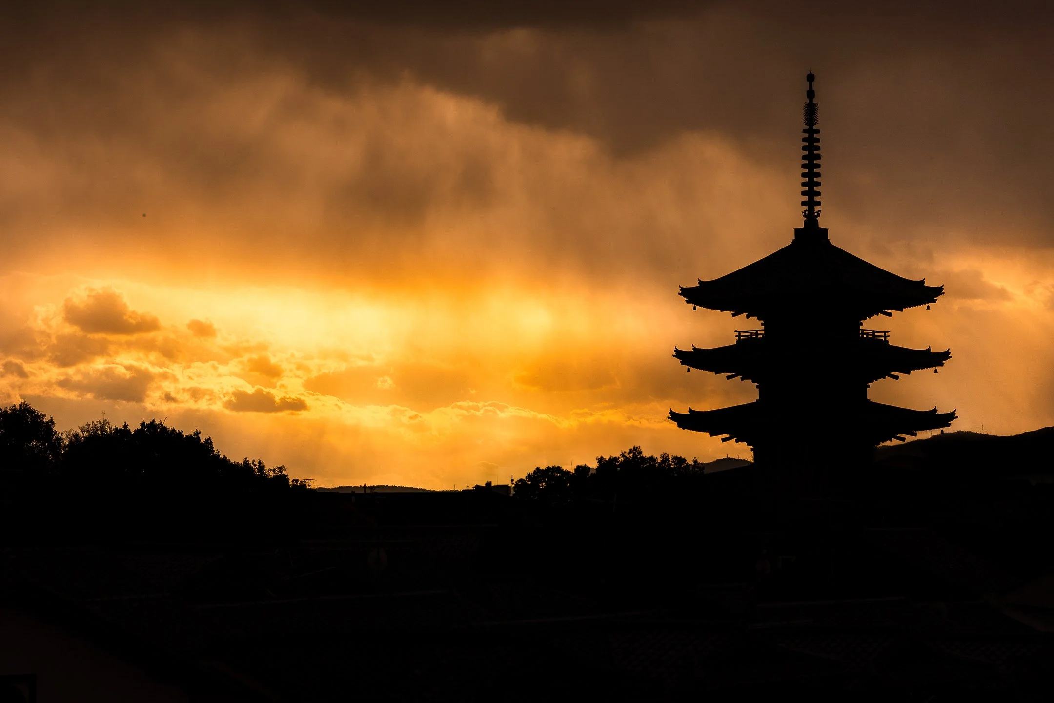 Silhouette d'un temple japonais traditionnel contre un ciel orageux au coucher du soleil.