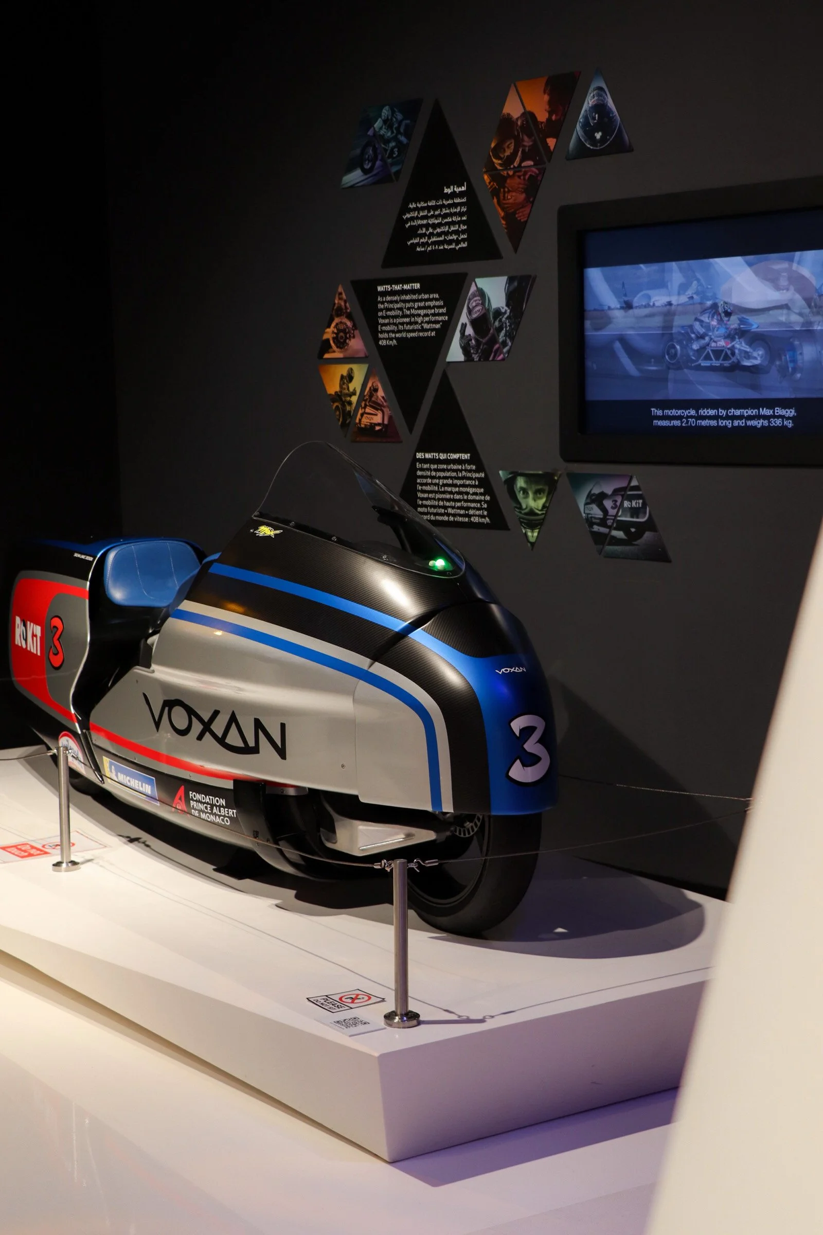 Une moto de course de l'équipe VoXAN exposée dans un musée, avec une signalétique en arrière-plan décrivant ses caractéristiques et sa performance.