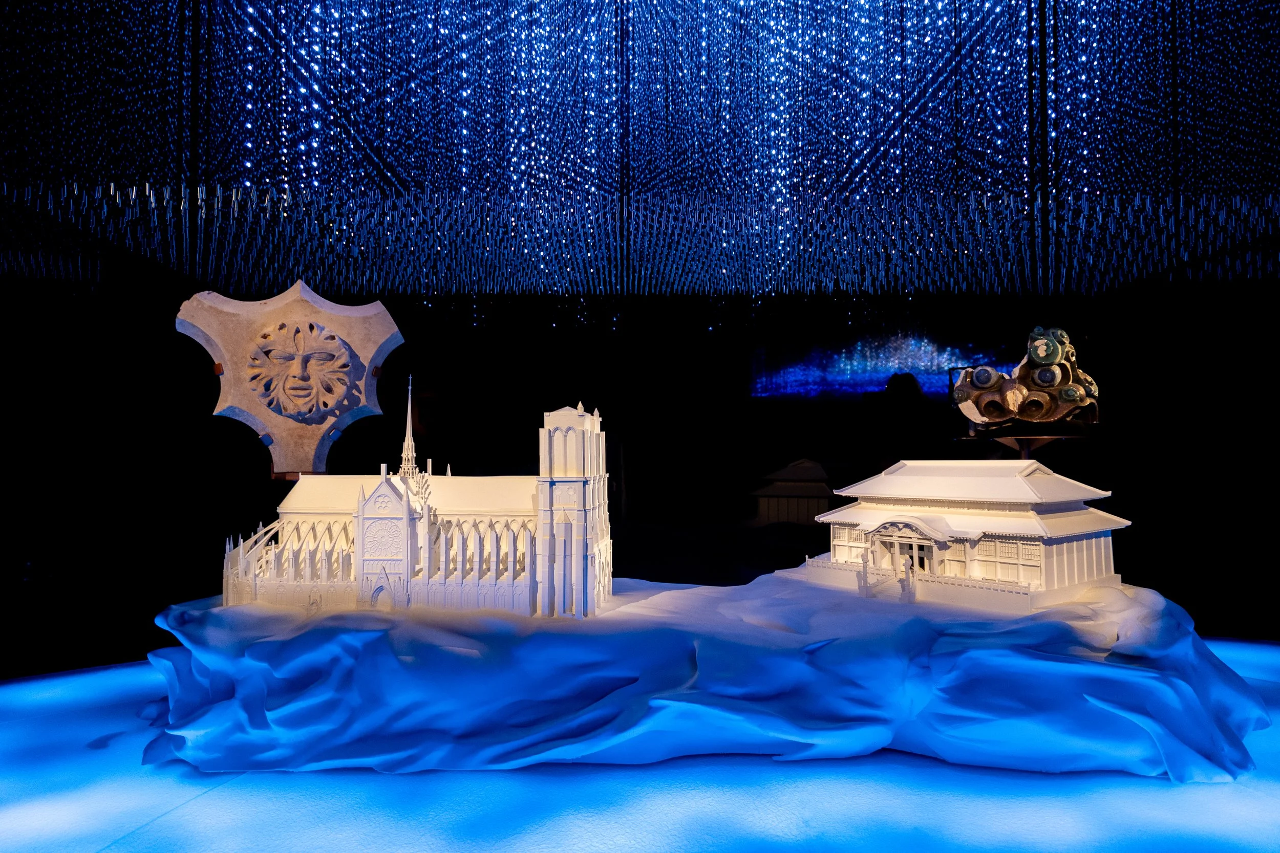 Modèle réduit de bâtiments architecturaux sous un plafond bleu illuminé avec des motifs de lumières scintillantes.