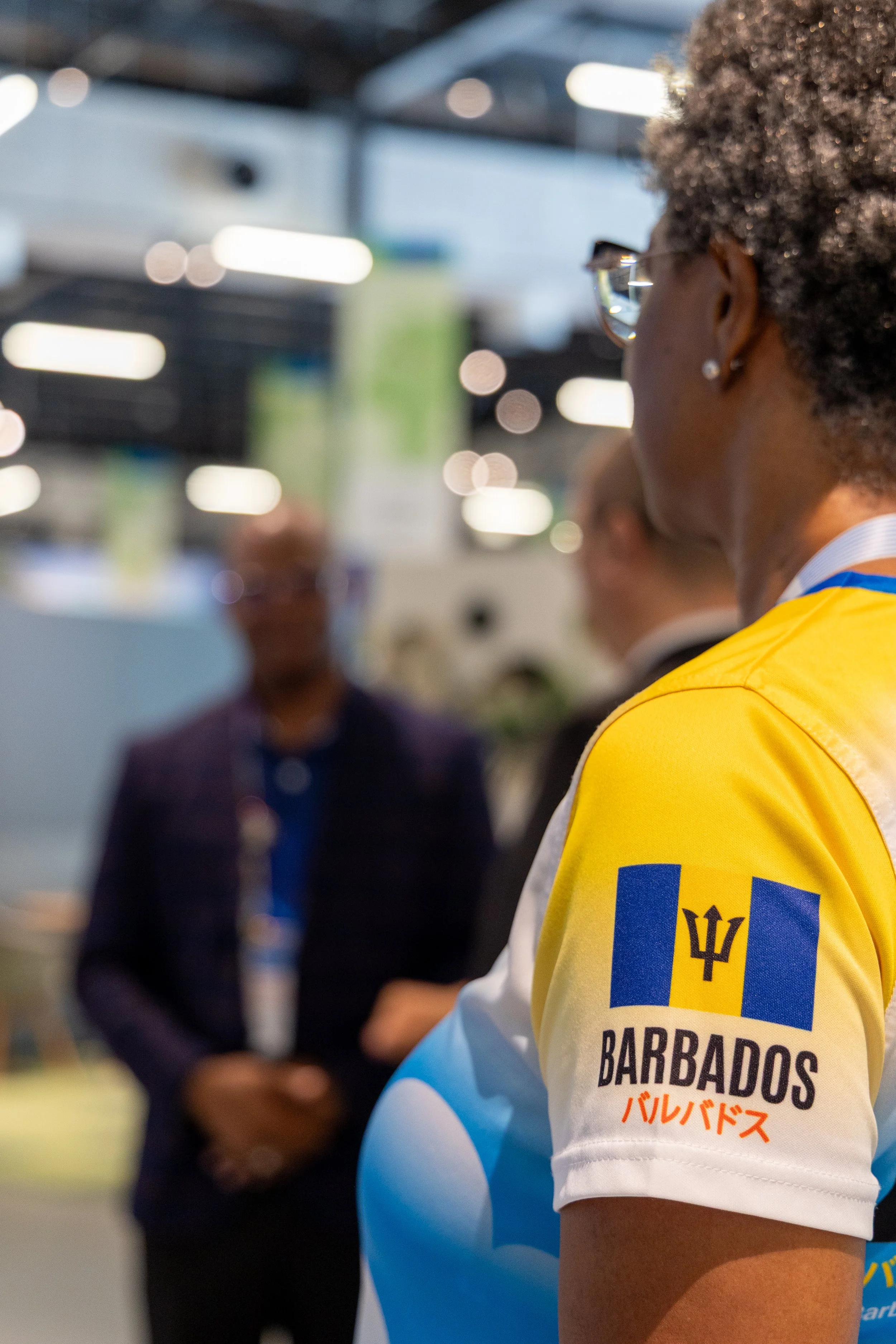 Une personne porte un t-shirt de sport avec le drapeau de la Barbade et le texte 'Barbados' écrit dessus, lors d'un événement ou d'une exposition.