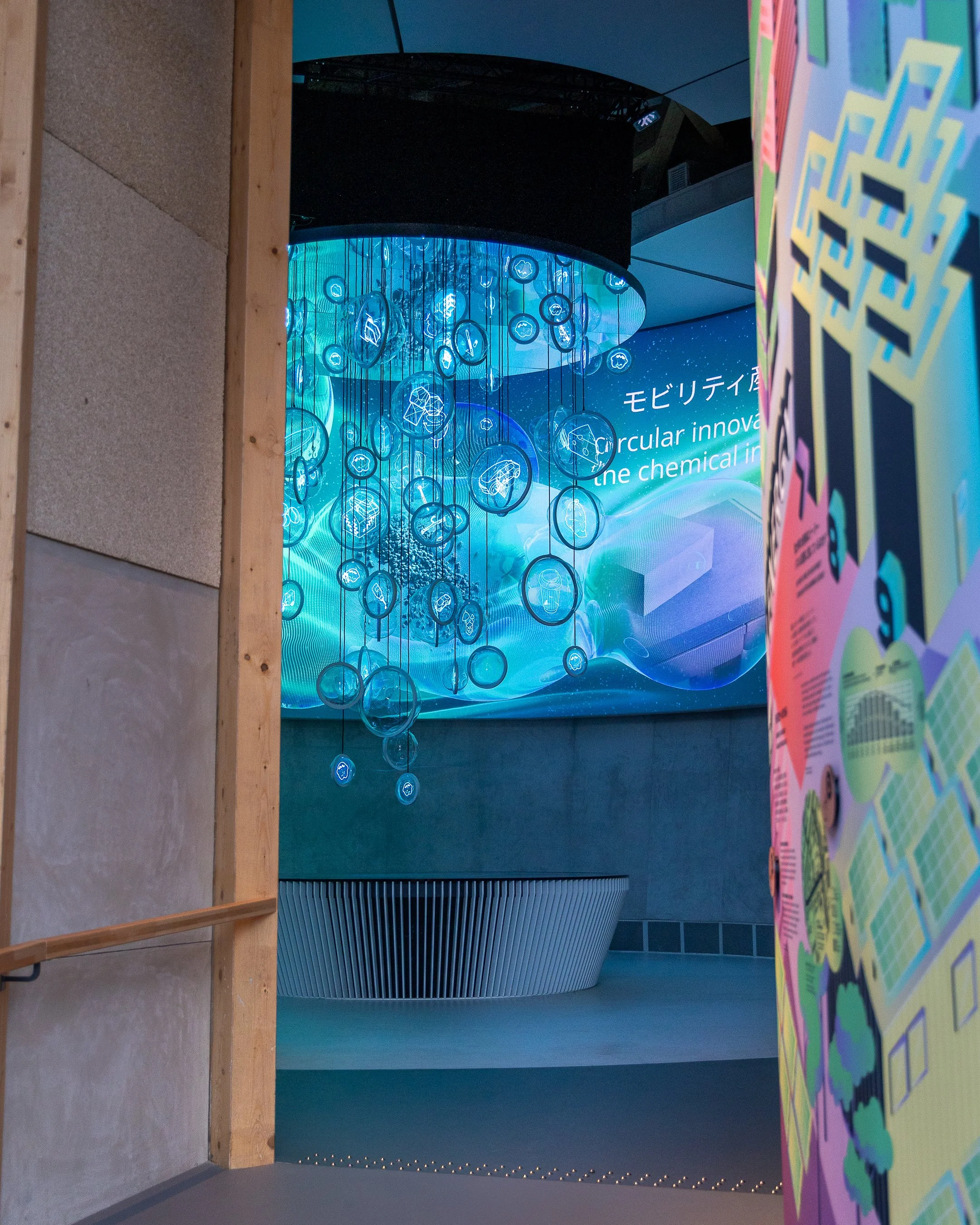 Une installation artistique avec de nombreuses sphères en verre suspendues, éclairées en bleu, représentant des formes de la science ou de la technologie, dans un espace sombre avec un fond numérique ou spatial.