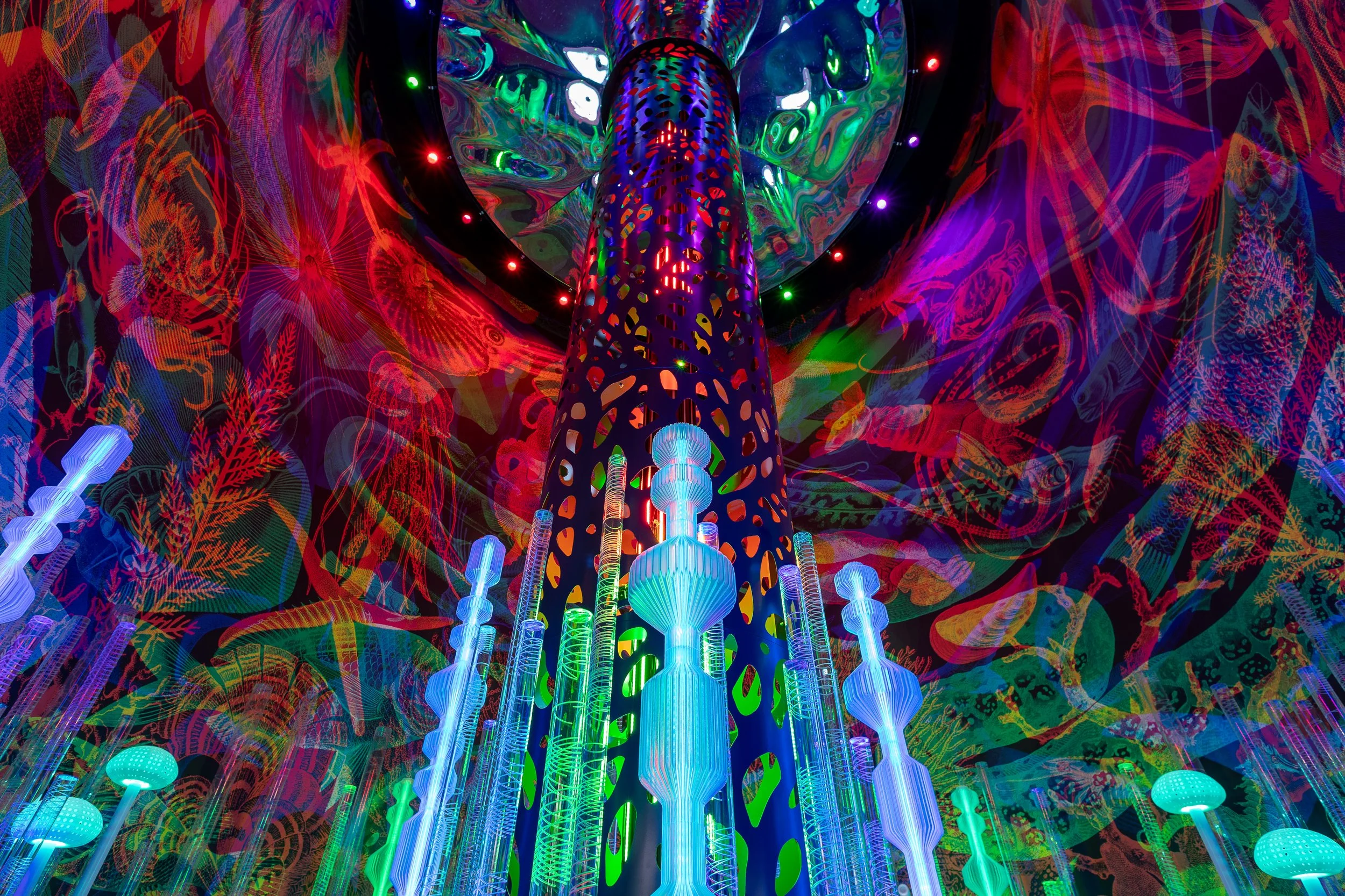 Une structure d'art futuriste avec des colonnes éclairées aux lumières fluorescentes bleues, entourée de décorations de style végétal phosphorescent en couleurs vives, dans un environnement intérieur aux couleurs néon.