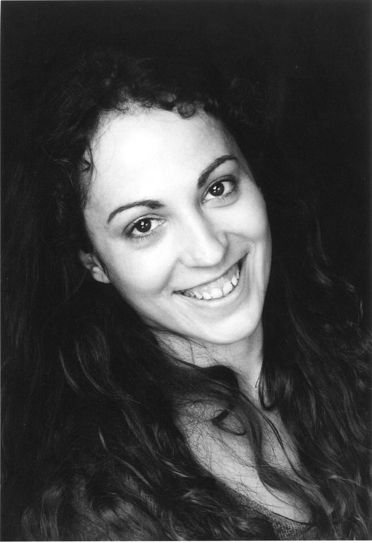 Black and white portrait of a woman with long wavy hair, smiling and looking at the camera.