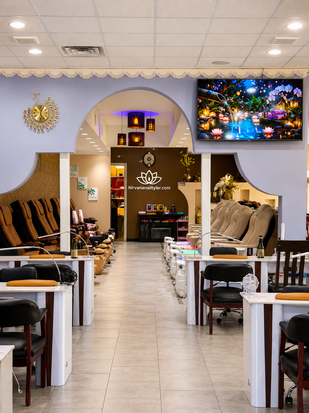 A nail salon with pedicure chairs along both sides, a reception area at the end, decorative lighting, and a large screen TV on the wall.