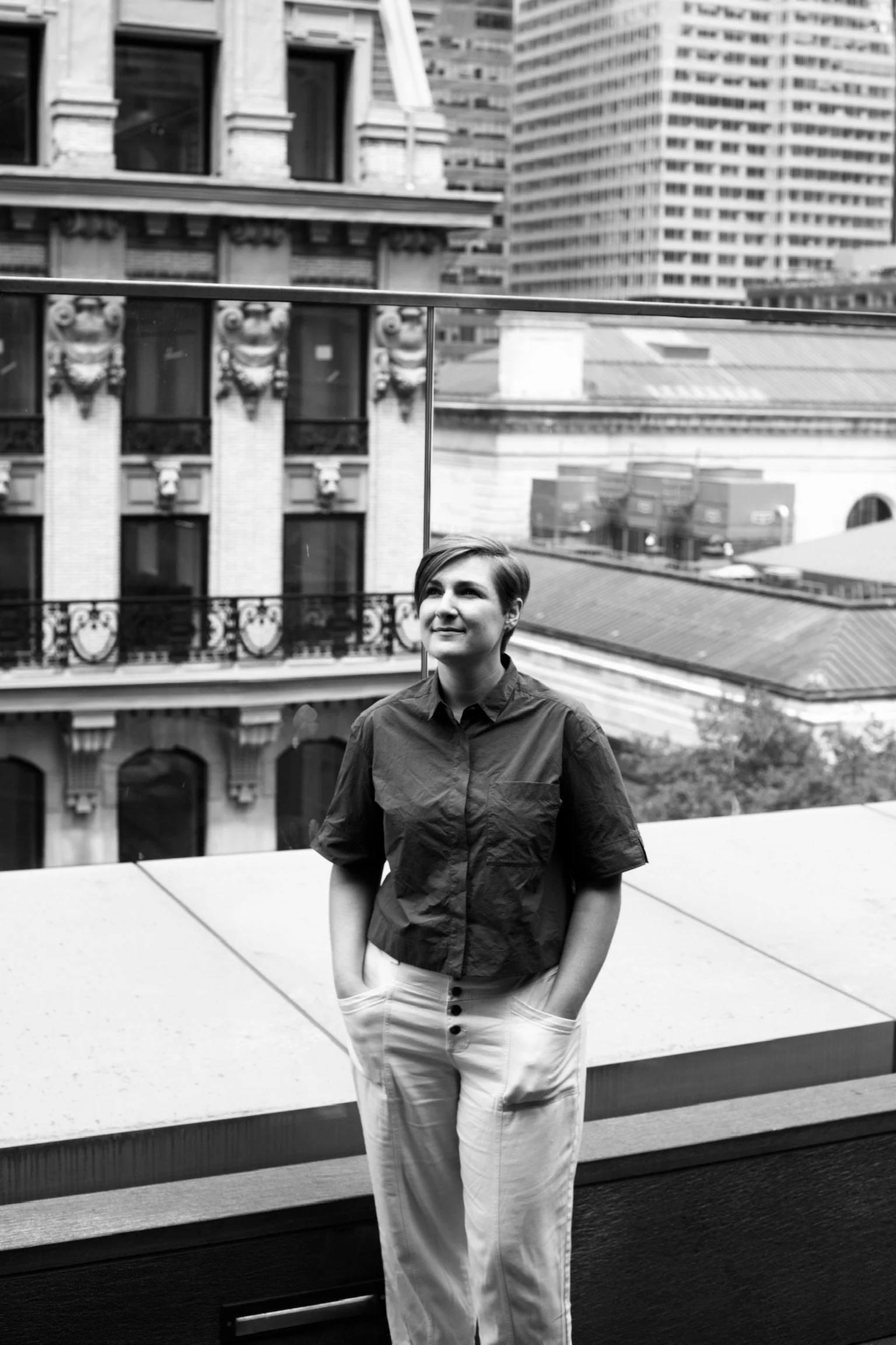 a black and white photo of Leya smiling, her hands in her pockets, surrounded by New York city buildings