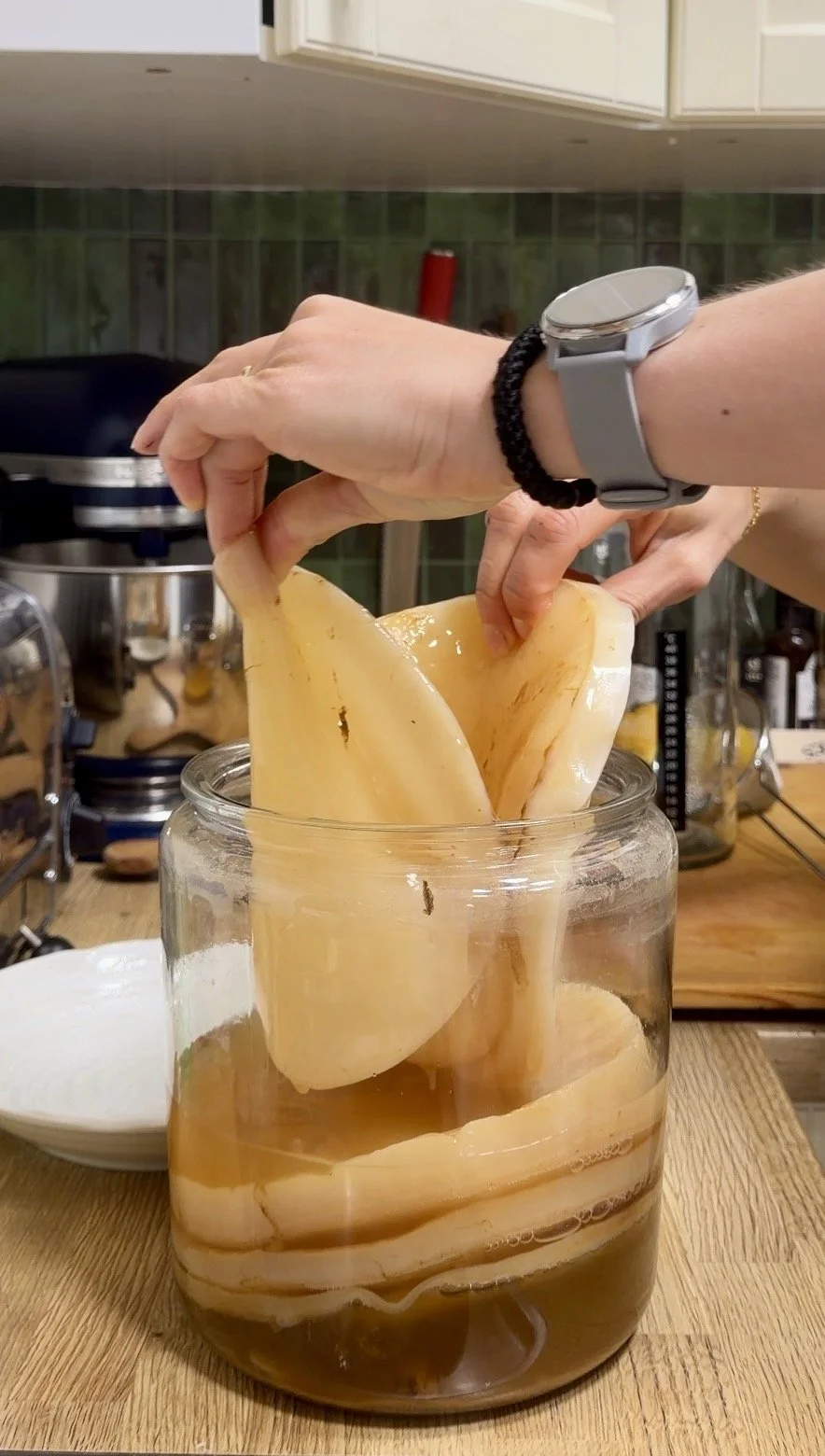 A person lifting a large piece of cheese from a jar filled with liquid in a kitchen.