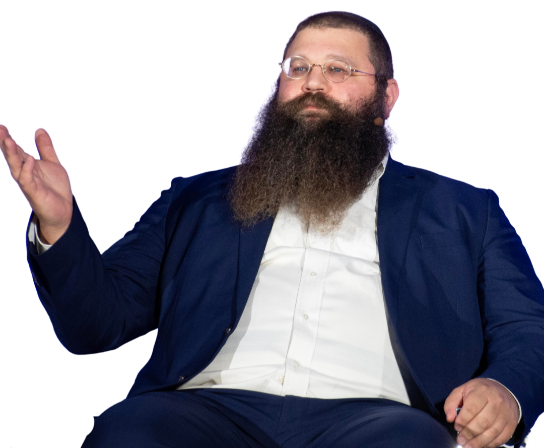 A man with glasses and a long beard wearing a navy blue suit and white shirt, gesturing with his hand.