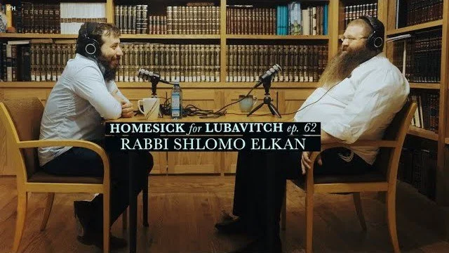 Bentzi Avtzon and Shlomo Elkan with headphones sitting at a table in a library or study room with bookshelves in the background, engaged in a conversation for a podcast titled "HOMESICK for LUBAVITCH ep. 62 RABBI SHLOMO ELKANA."