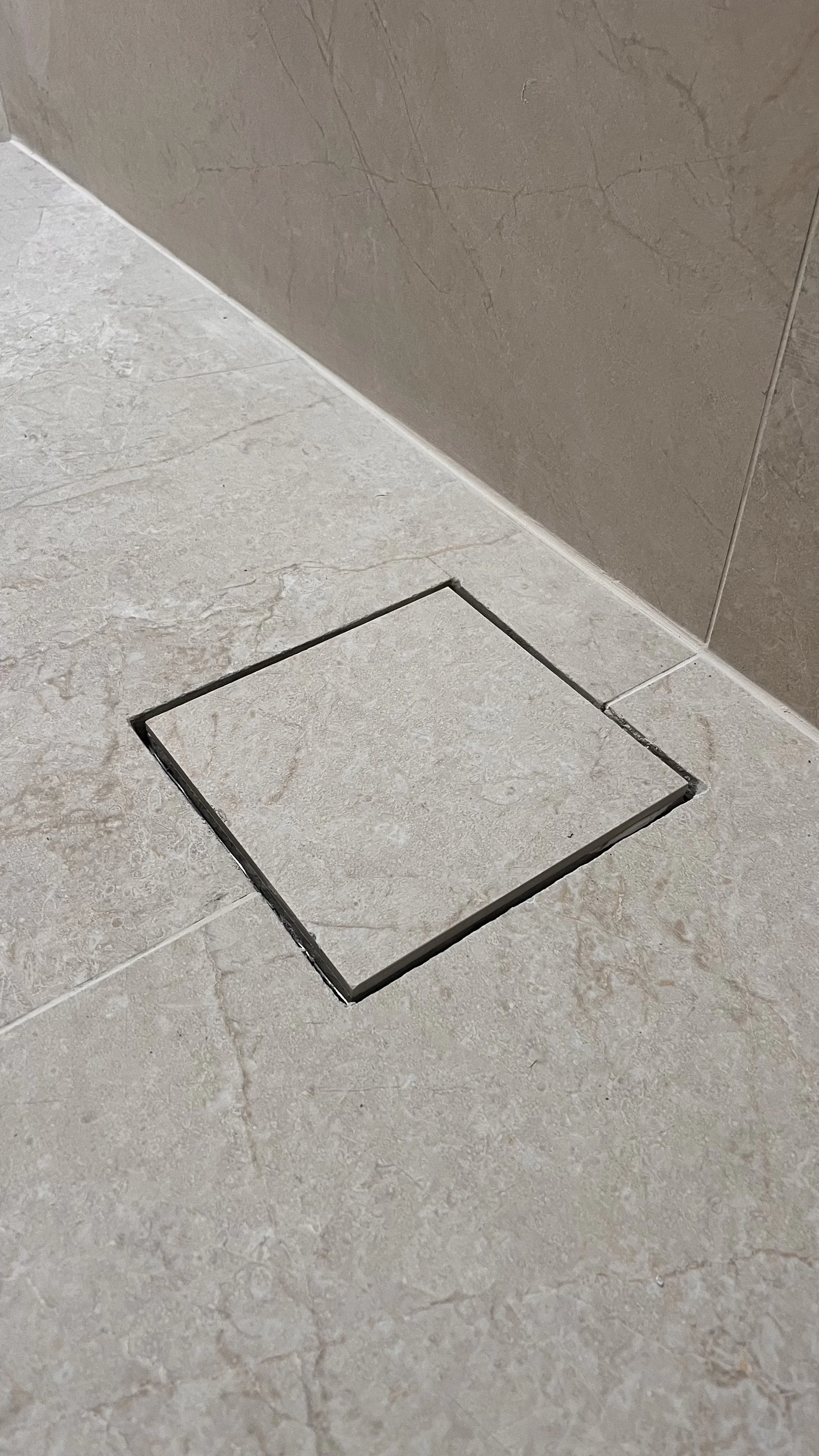 Rejunte preto ao redor de um ralo quadrado em piso de mármore bege claro.