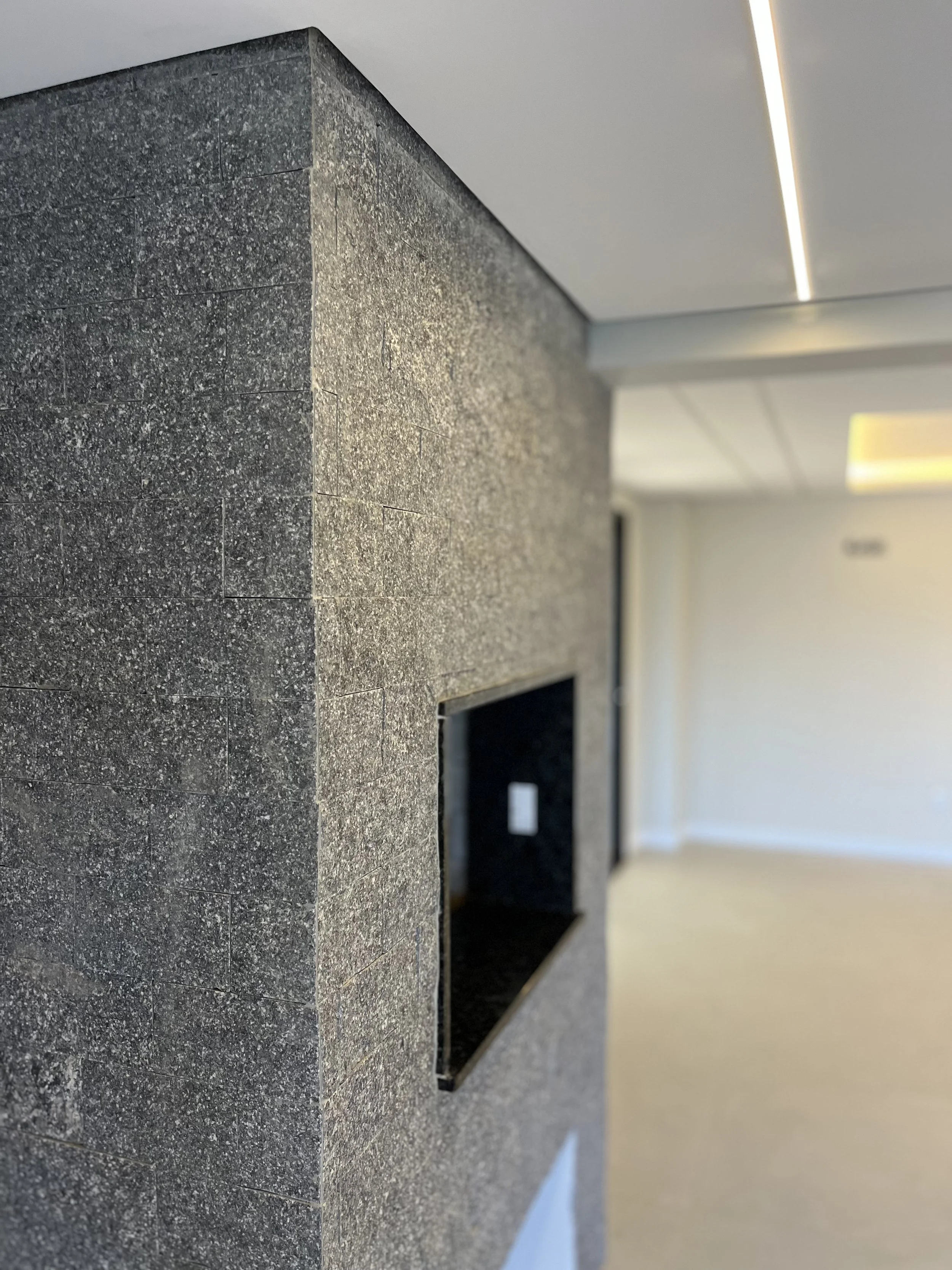 Pared de pedra pretas na parede de uma sala com teto branco e iluminação embutida.