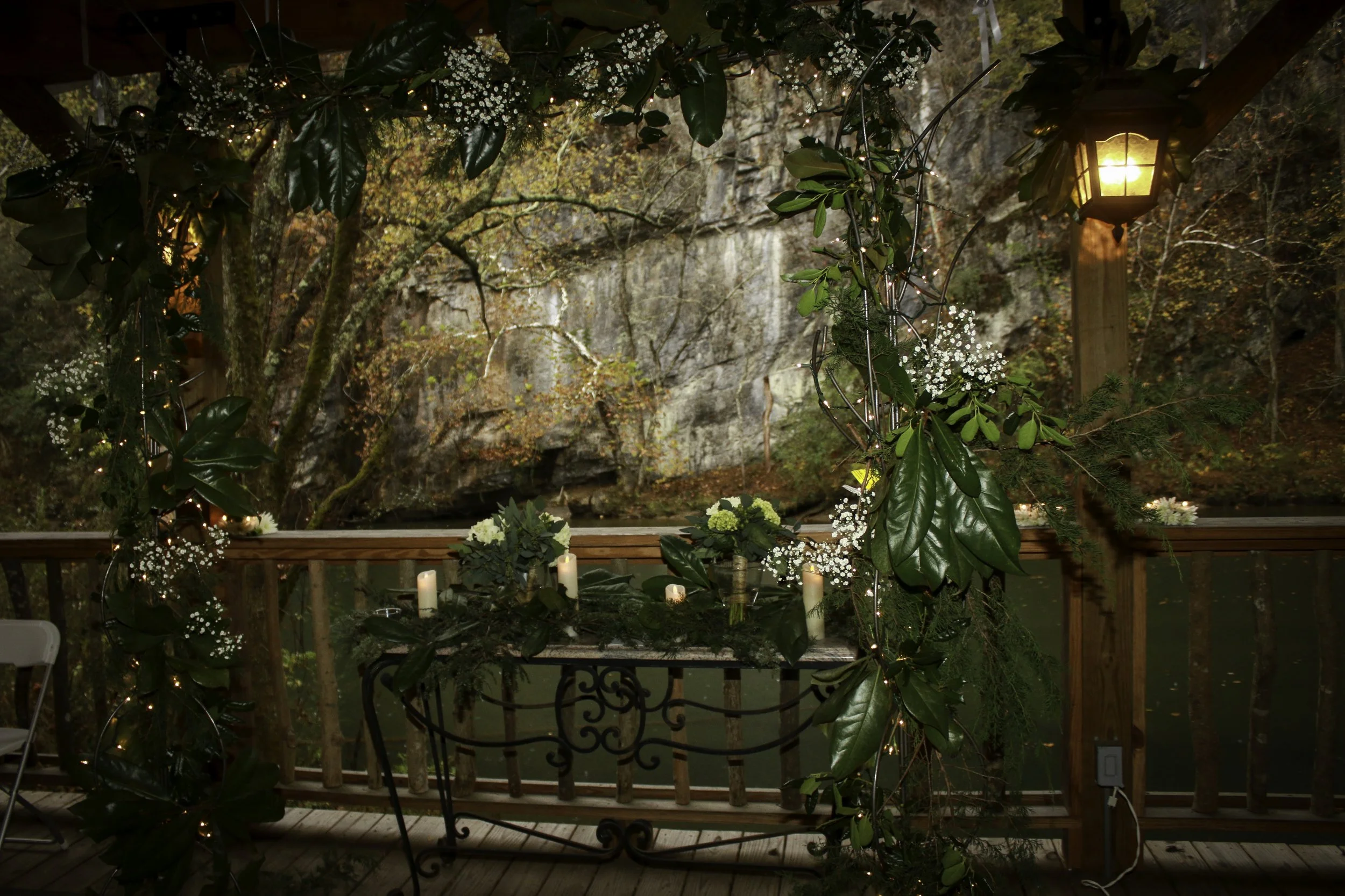 Twinkle-light wedding ceremony arch with greenery and candles against a rock wall backdrop, planned by Well Gathered in Eastern TN